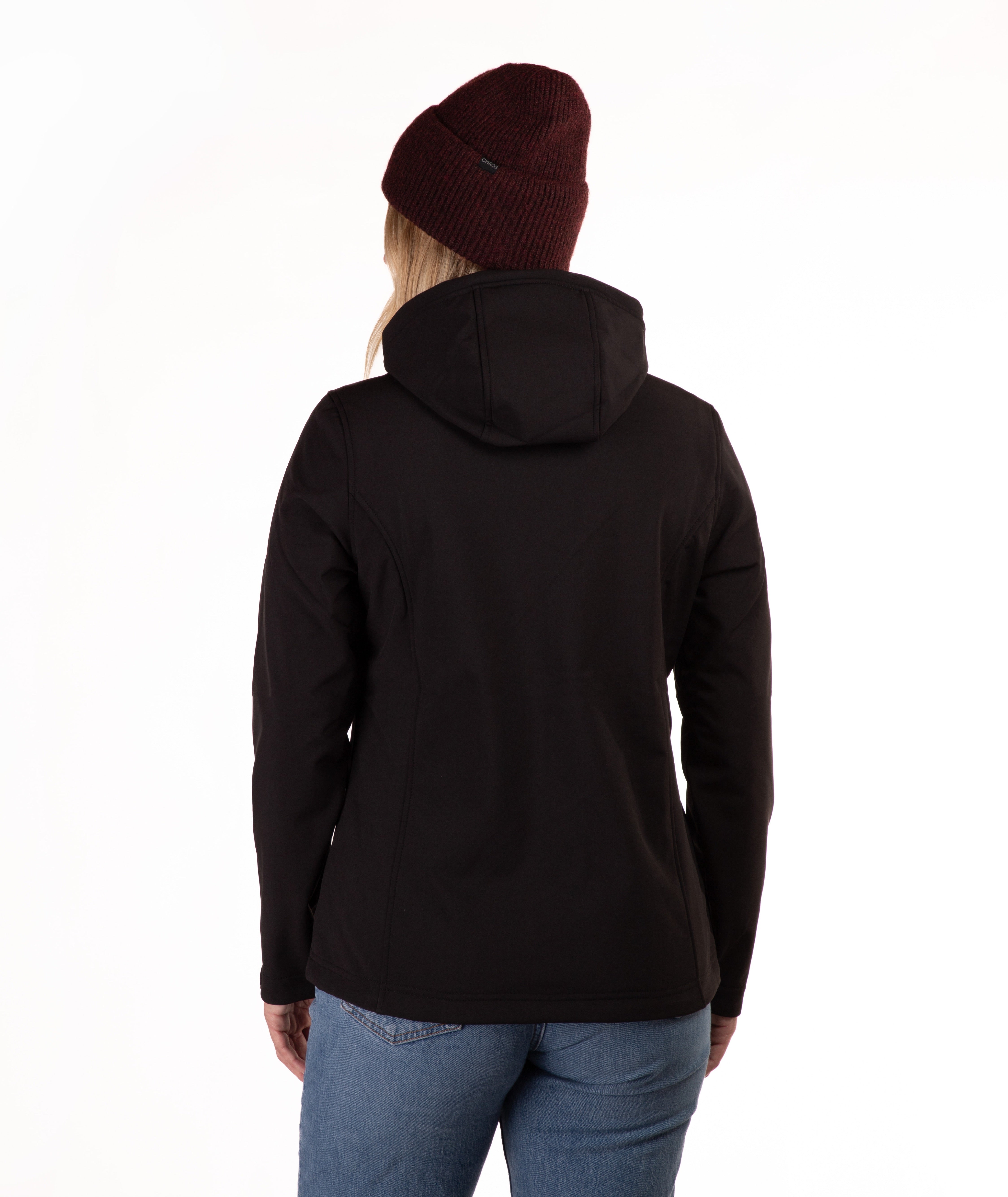 A woman viewed from the back wearing a black hooded jacket, a dark burgundy knit beanie, and blue jeans against a plain white studio background.