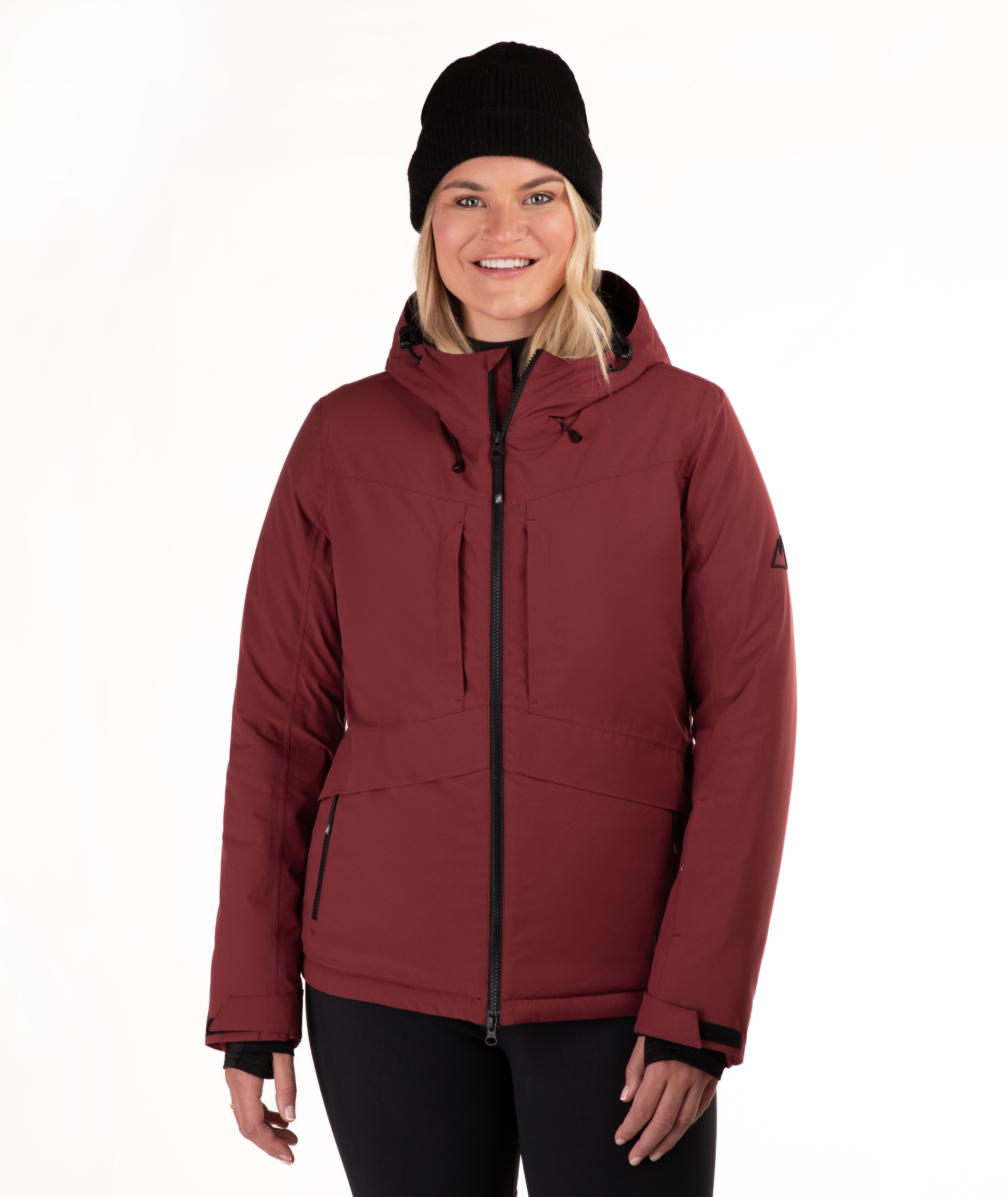 A woman wearing a dark red hooded ski jacket, a black knit beanie, and black pants, standing against a plain white studio background.