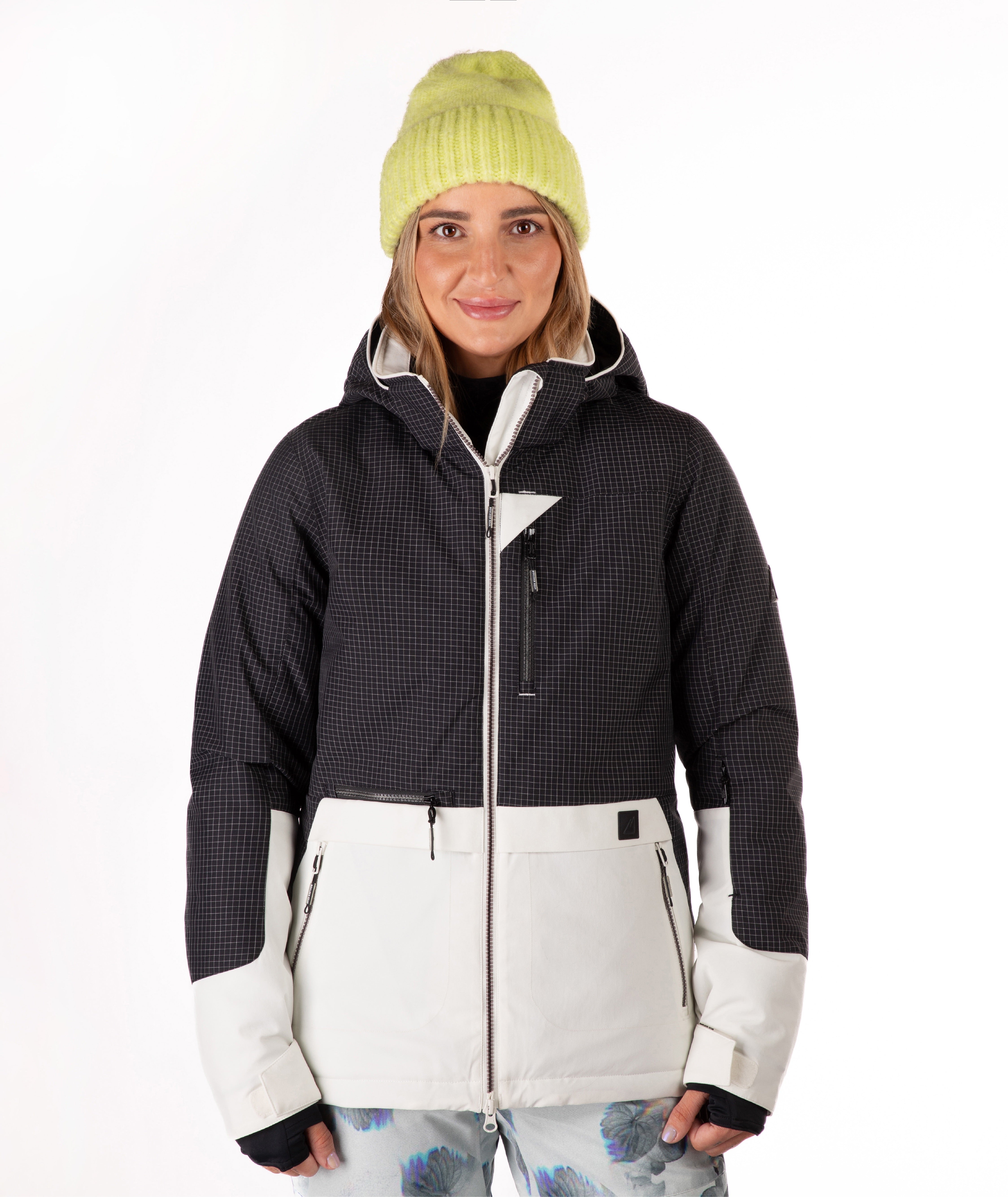 A woman modeling a women's ski jacket with a black and white grid pattern, paired with a light yellow knit beanie, against a plain white background.