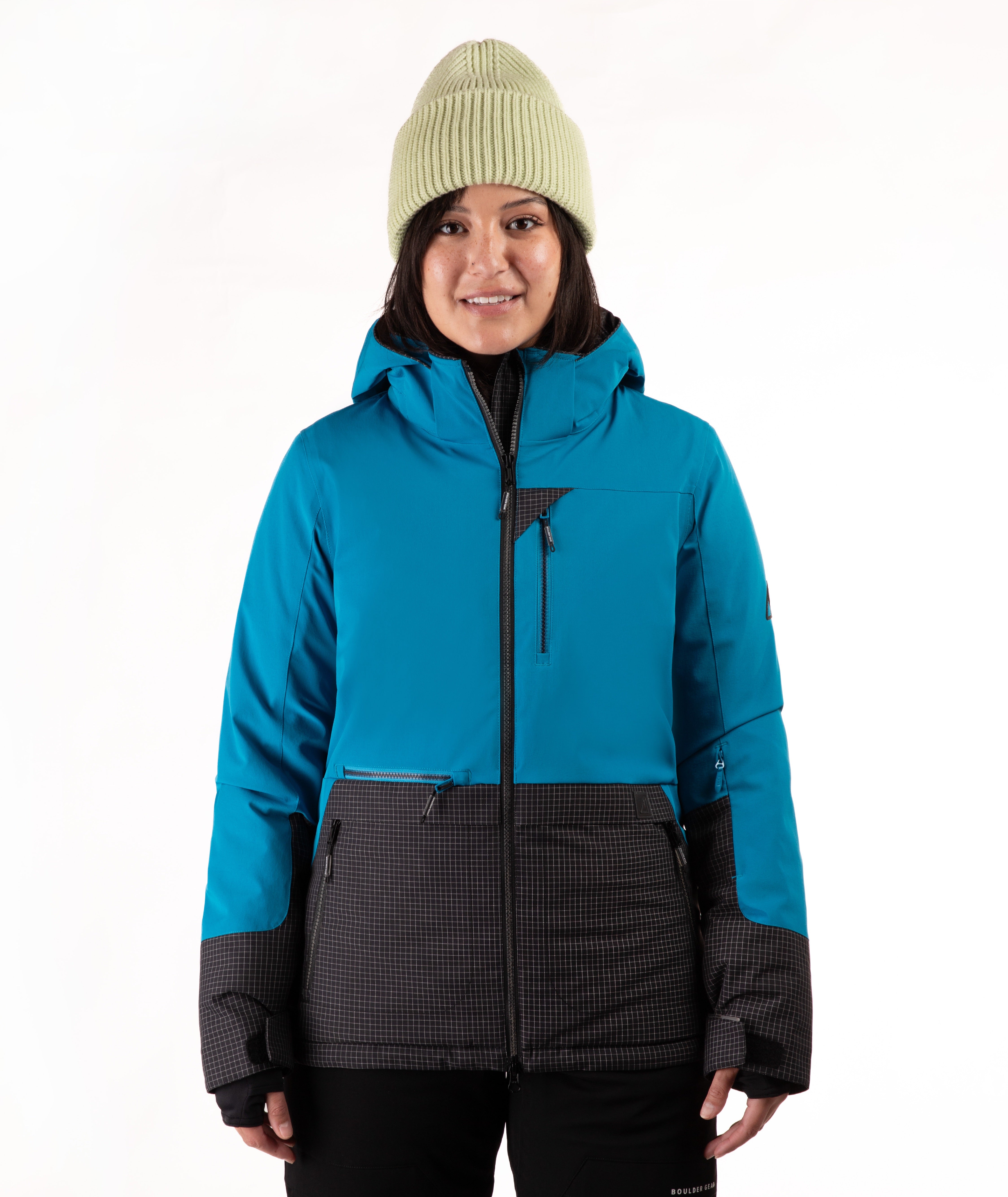 A woman wearing a bright turquoise and black check ski jacket with a green beanie, standing against a plain white background.