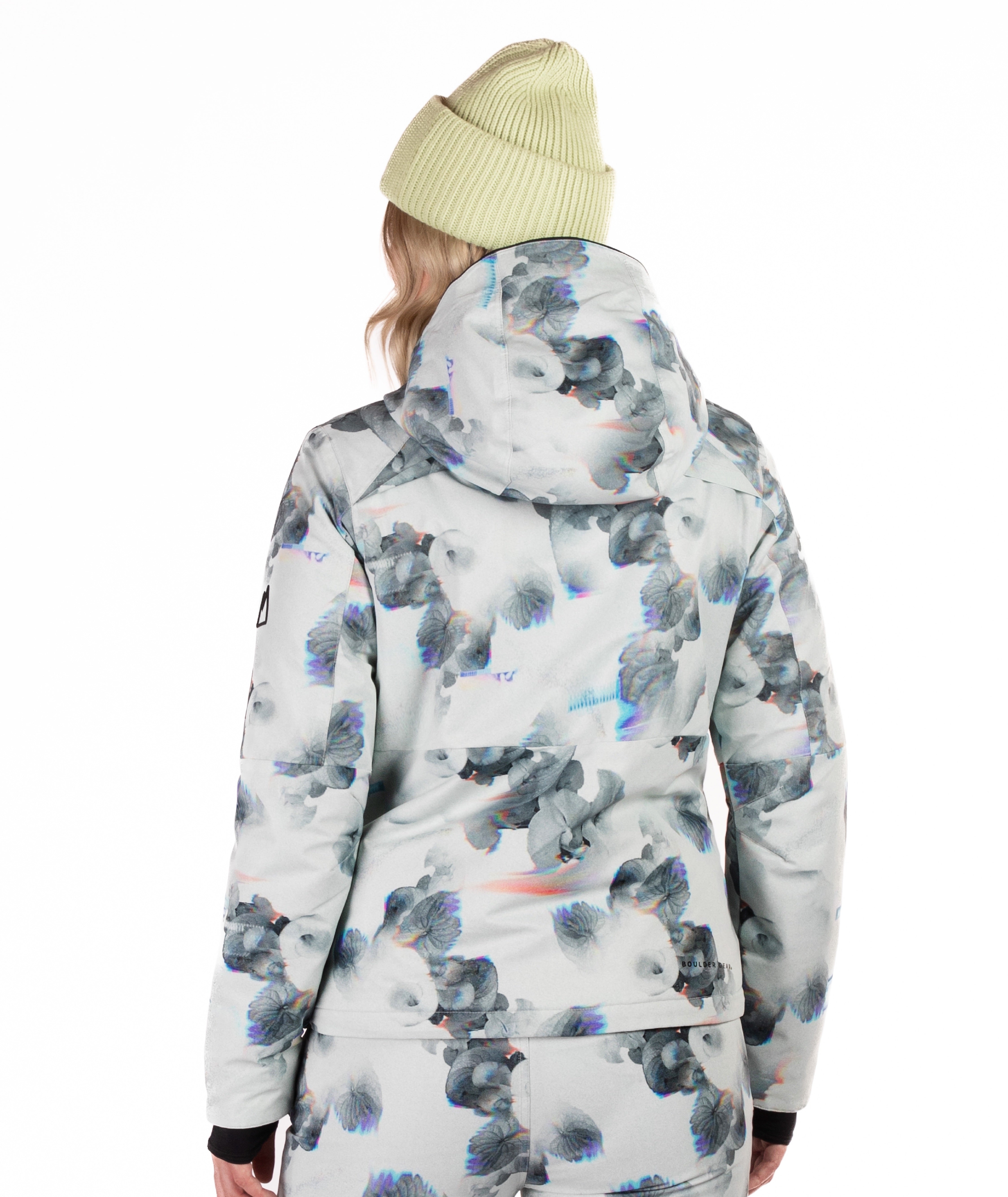 Person wearing a patterned snow jacket with black chest zippers on a white background highlighting the back of the jacket and the hood