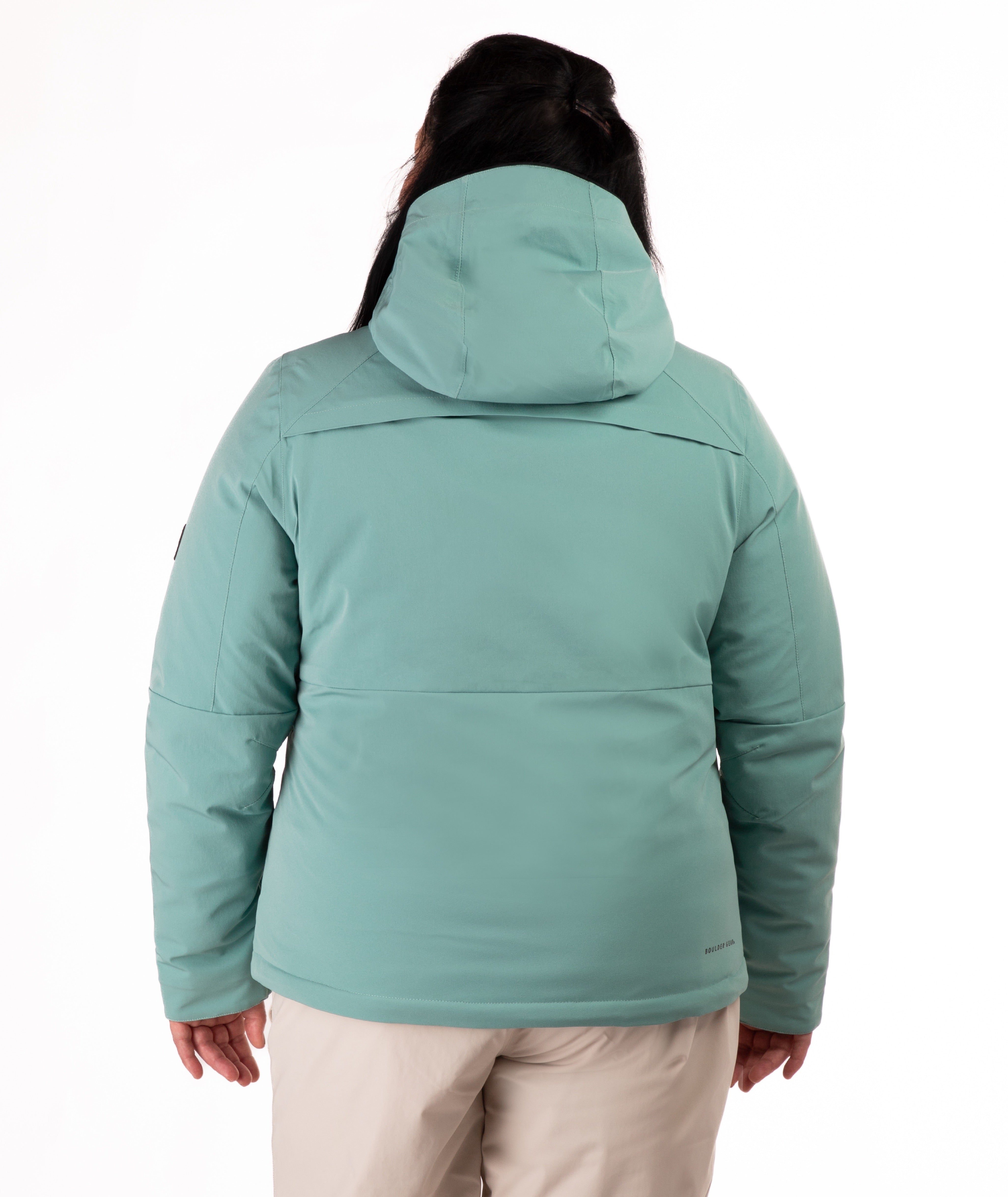Woman wearing a teal snow jacket with black chest zippers on a white background highlighting back of jacket and hood