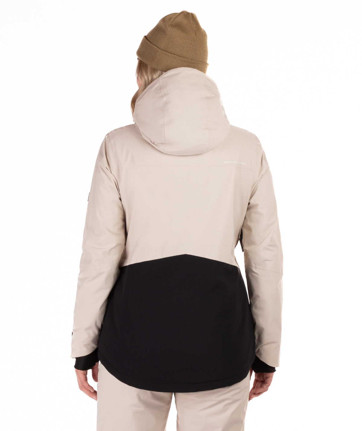 A person shown from the back wearing a color-blocked hooded jacket in light beige and black, with a tan beanie, against a plain white studio background.