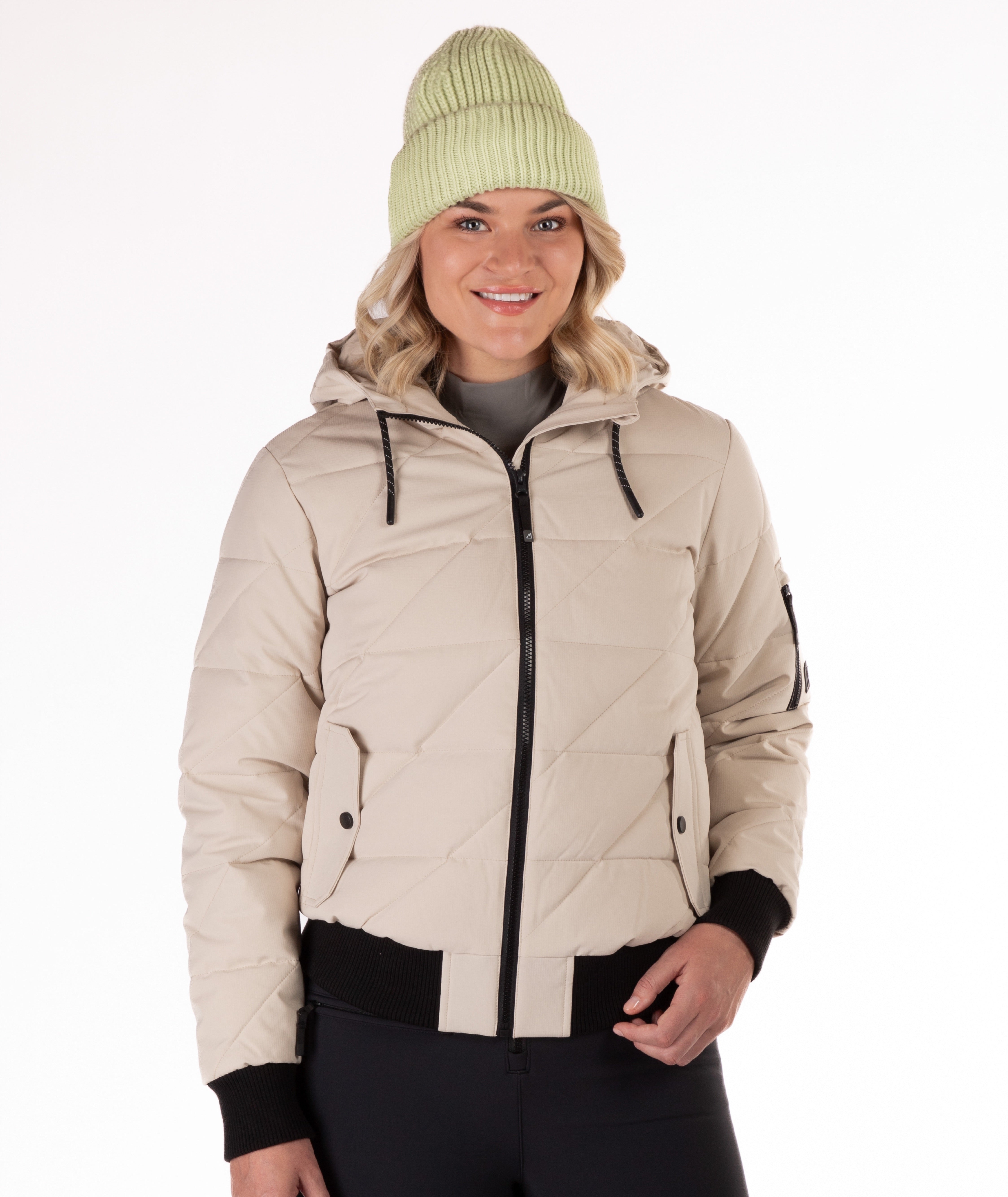 Woman wearing a beige quilted jacket with black knit trim on the sleeve cuffs and bottom hem on a white background.
