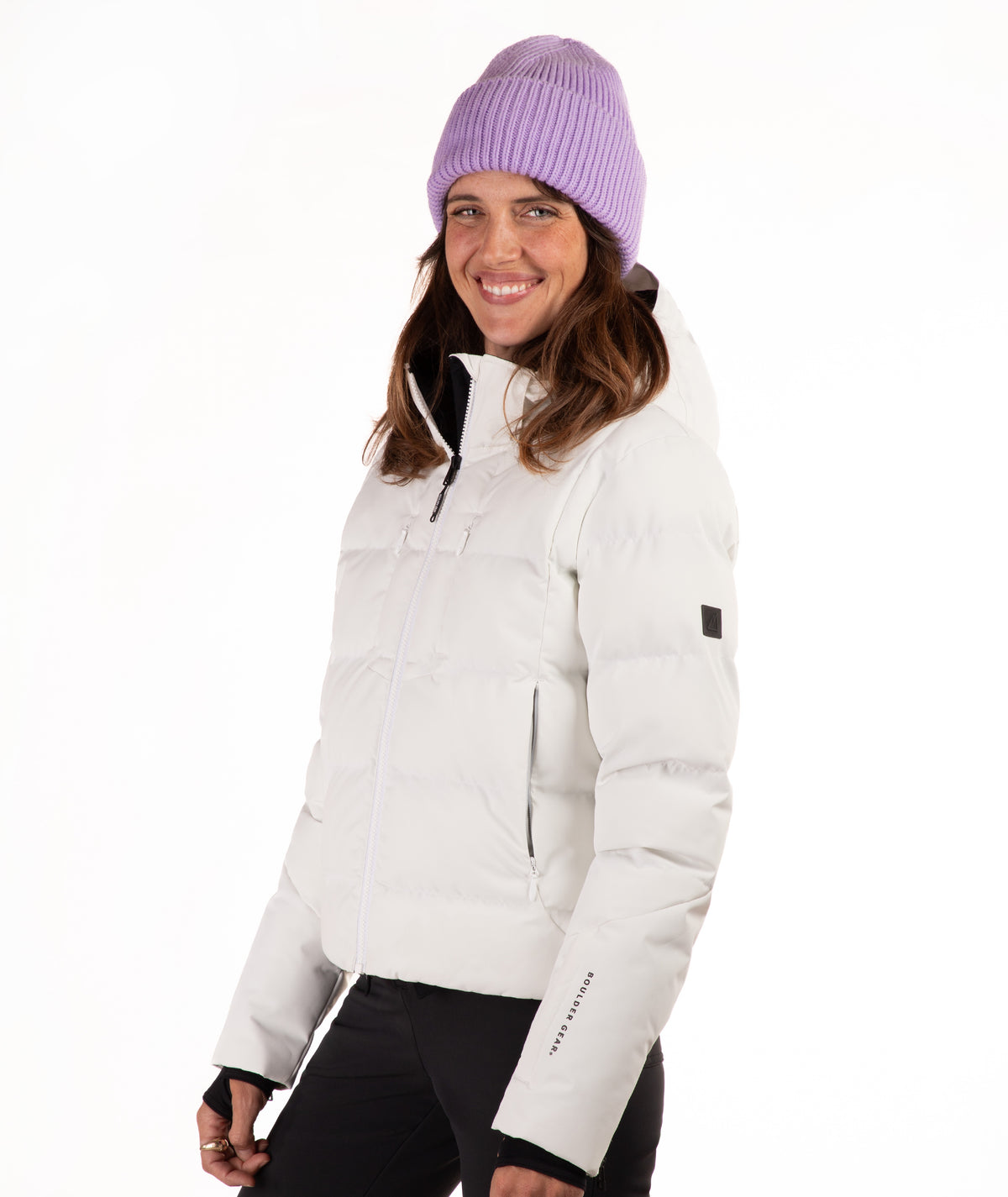 A woman wearing a off white puffer jacket and a lavender knit beanie, photographed against a clean white studio background.