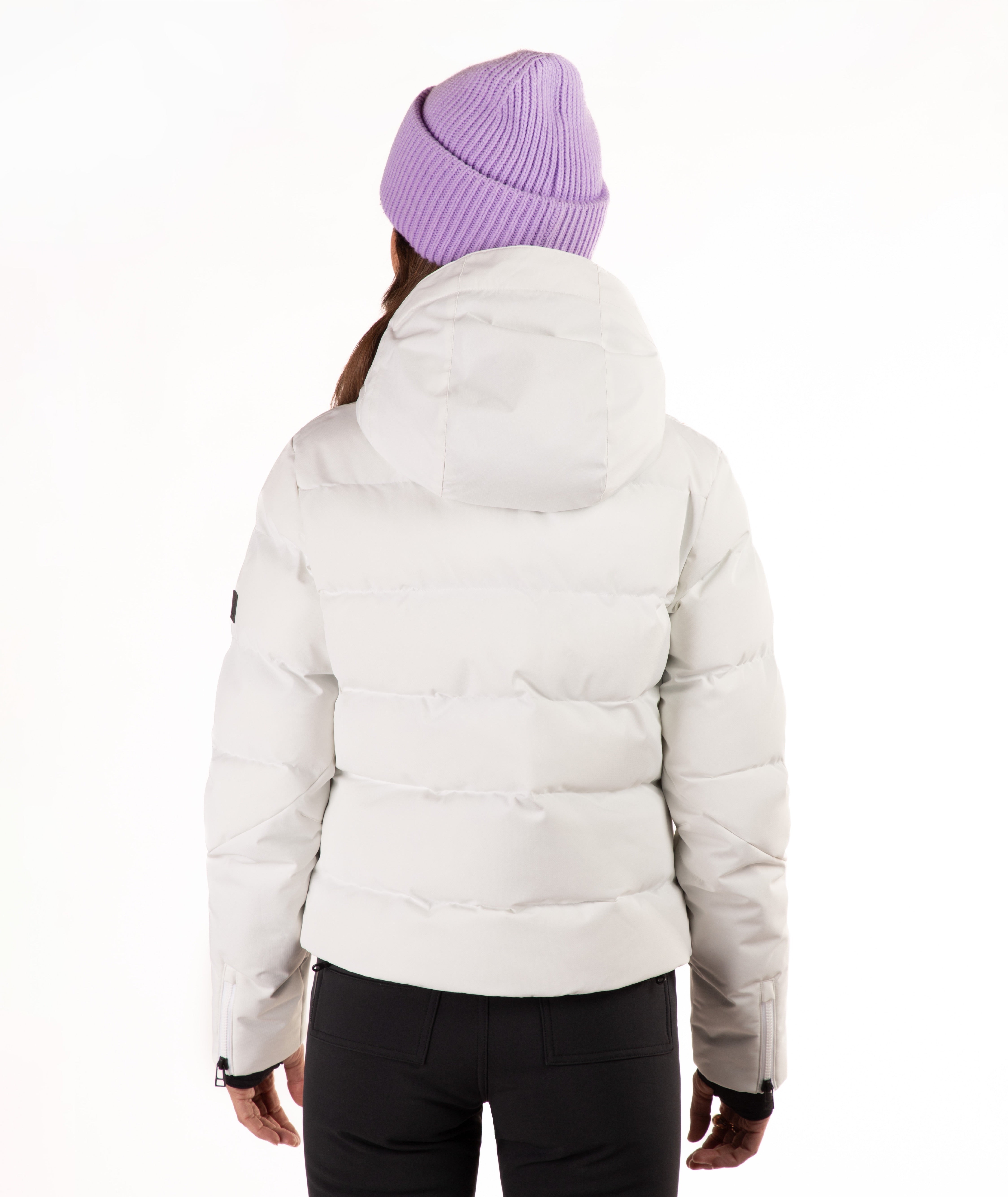 A person shown from the back wearing a light off-white puffer jacket, a lavender ribbed knit beanie, and black pants against a plain white studio background.
