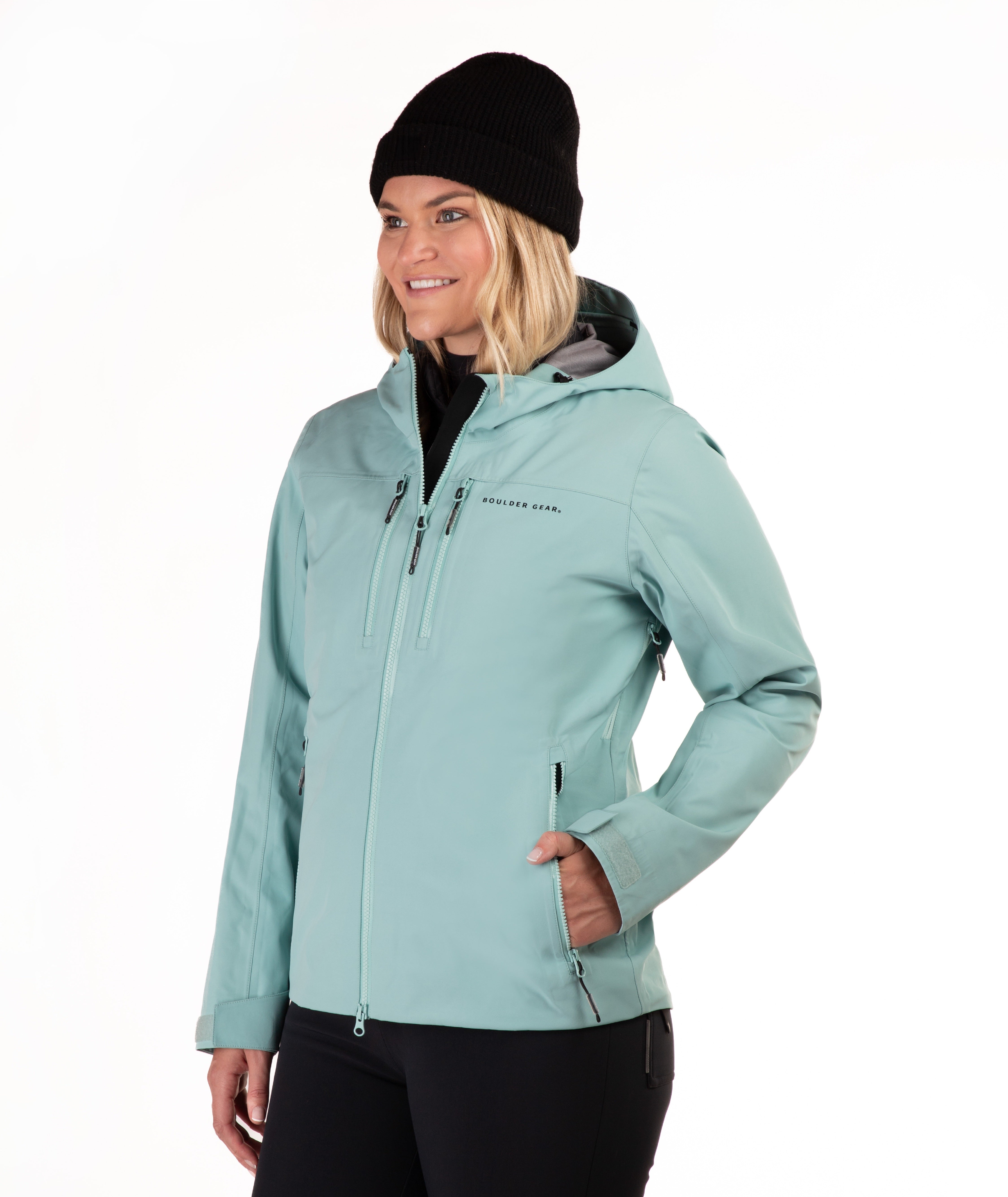 A woman wearing a light teal hooded ski jacket and black pants, paired with a black beanie, photographed against a plain white studio background.
