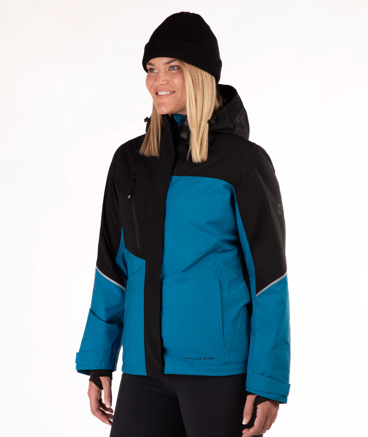 A woman wearing a black and teal ski jacket, black beanie, and black pants, photographed against a plain white studio background.
