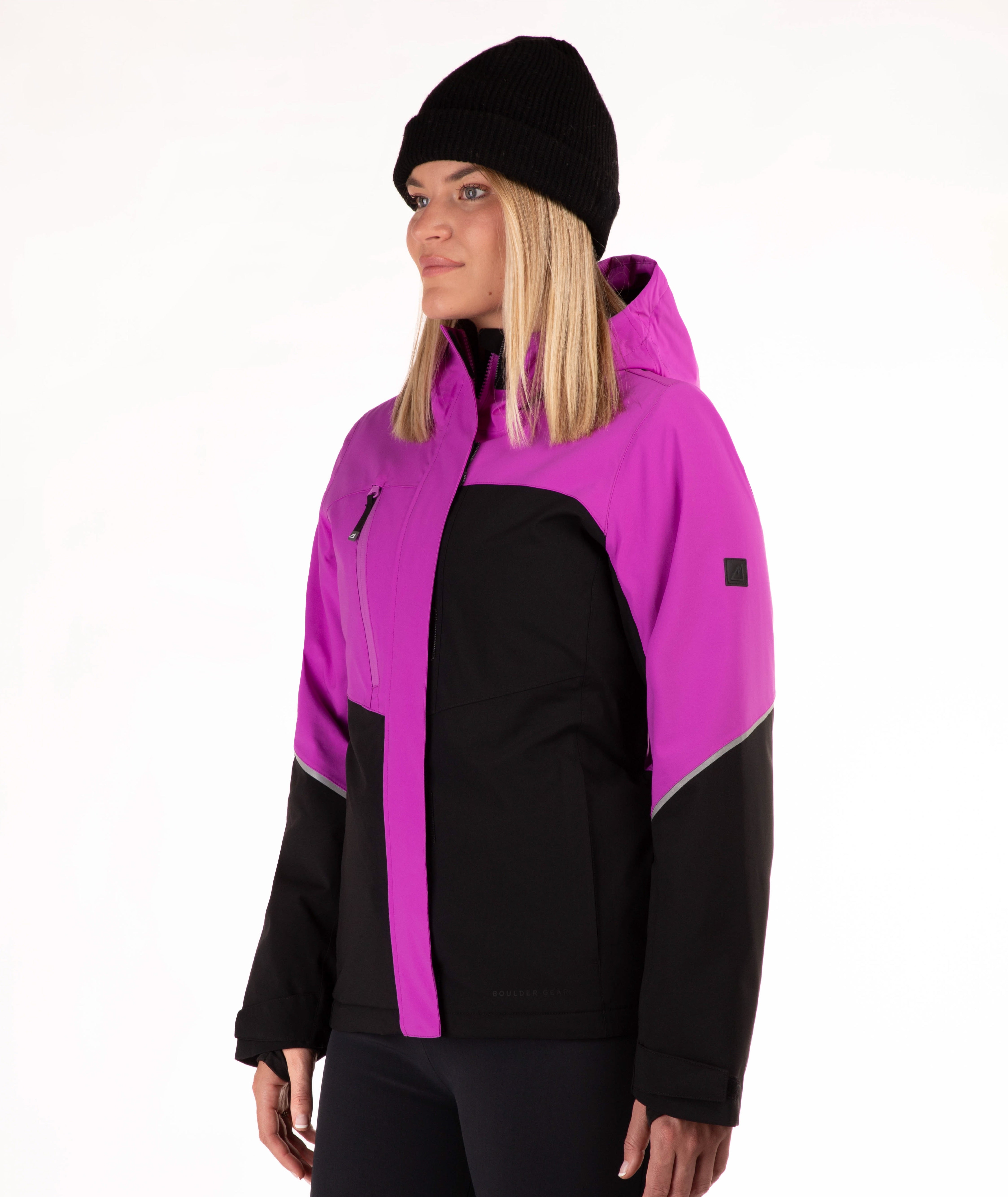 A woman wearing a bright magenta and black color-blocked ski jacket, a black beanie, and black pants, photographed against a plain white studio background.