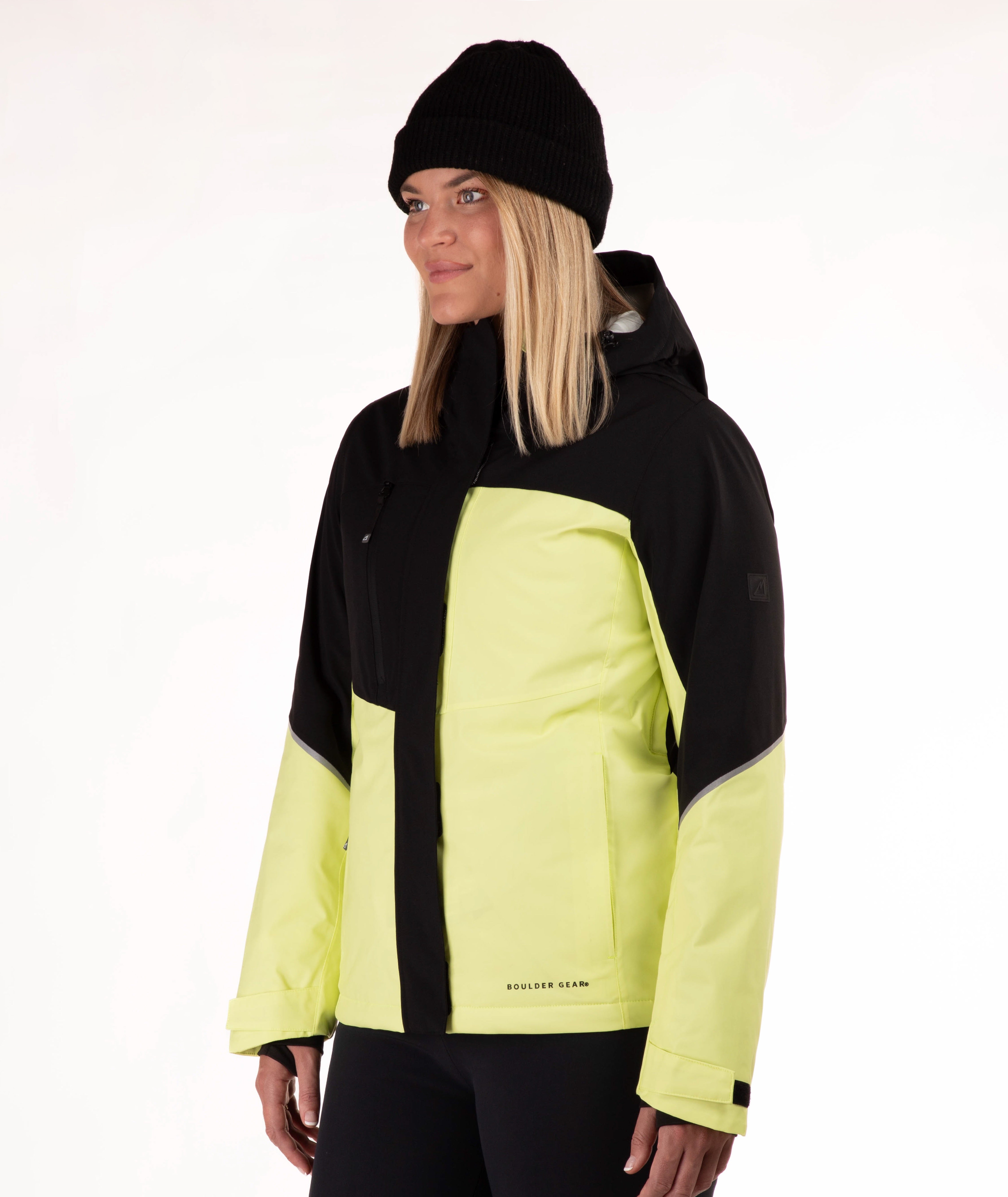 A woman wearing a black and light yellow ski jacket with a black beanie, photographed against a plain white studio background.