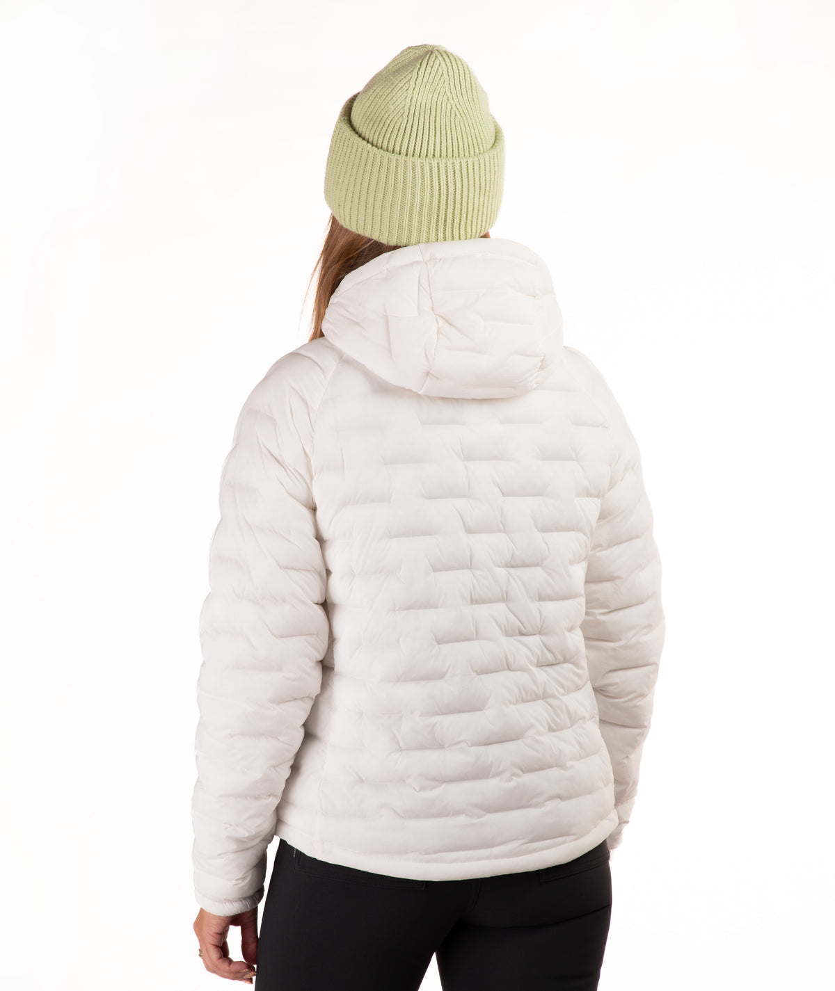 A person shown from the back wearing a off-white quilted puffer jacket with a hood, paired with a light green ribbed beanie and black pants, against a plain white studio background.