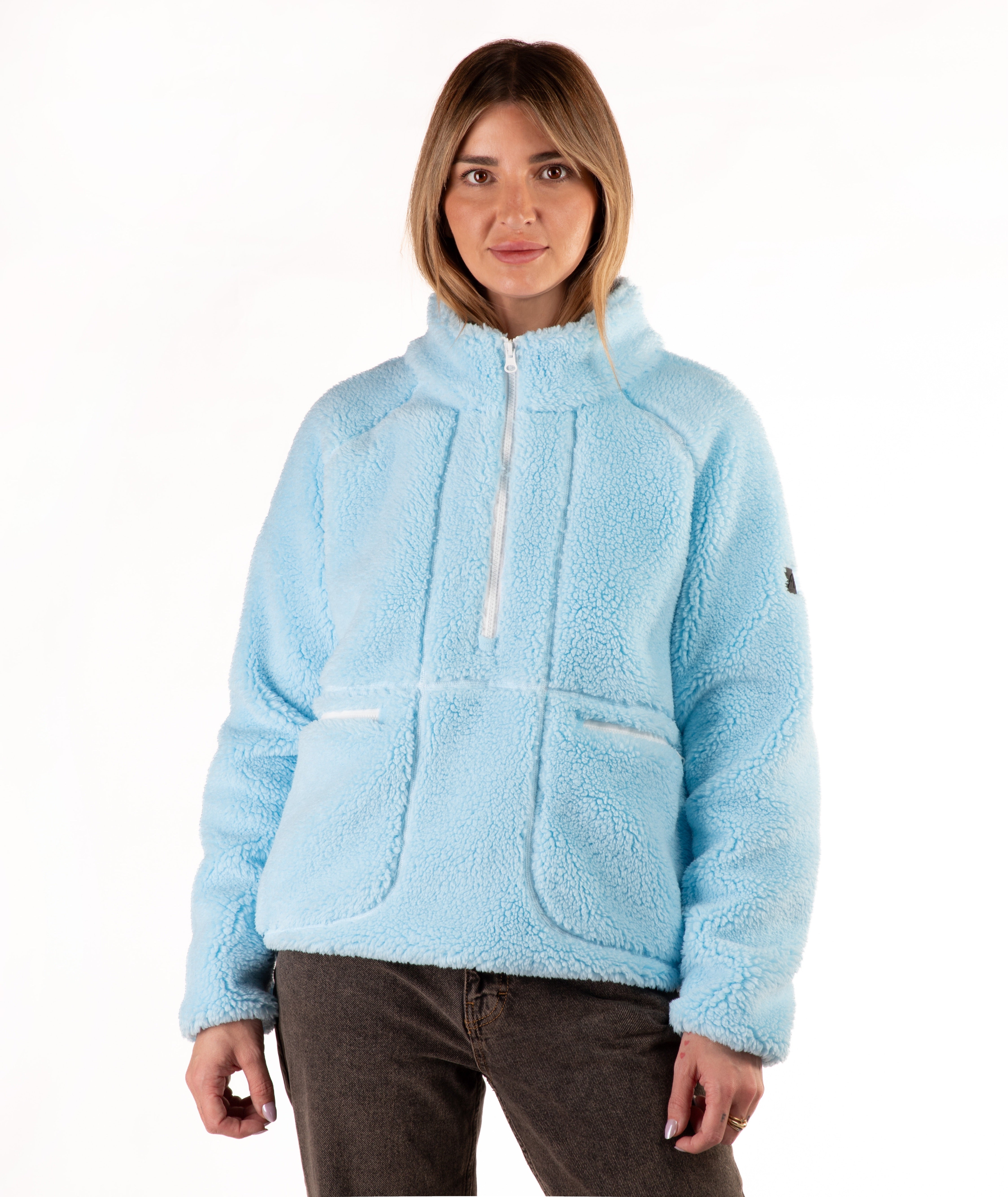A woman wearing a light blue sherpa fleece pullover jacket with a half-zip neckline and front patch pockets, paired with dark brown pants, against a plain white background.