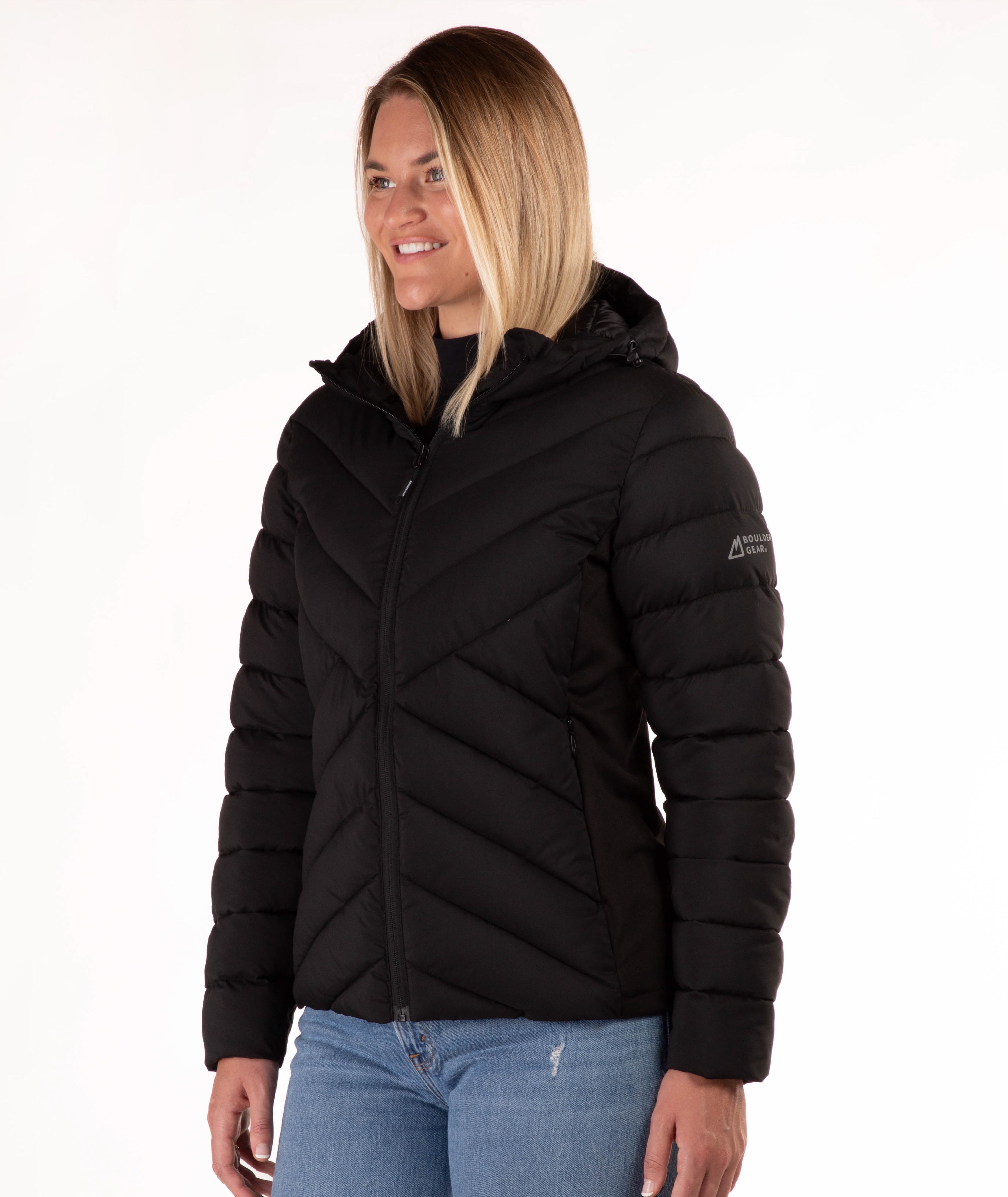 A woman wearing a black hooded puffer jacket paired with blue jeans, photographed against a plain white studio background.