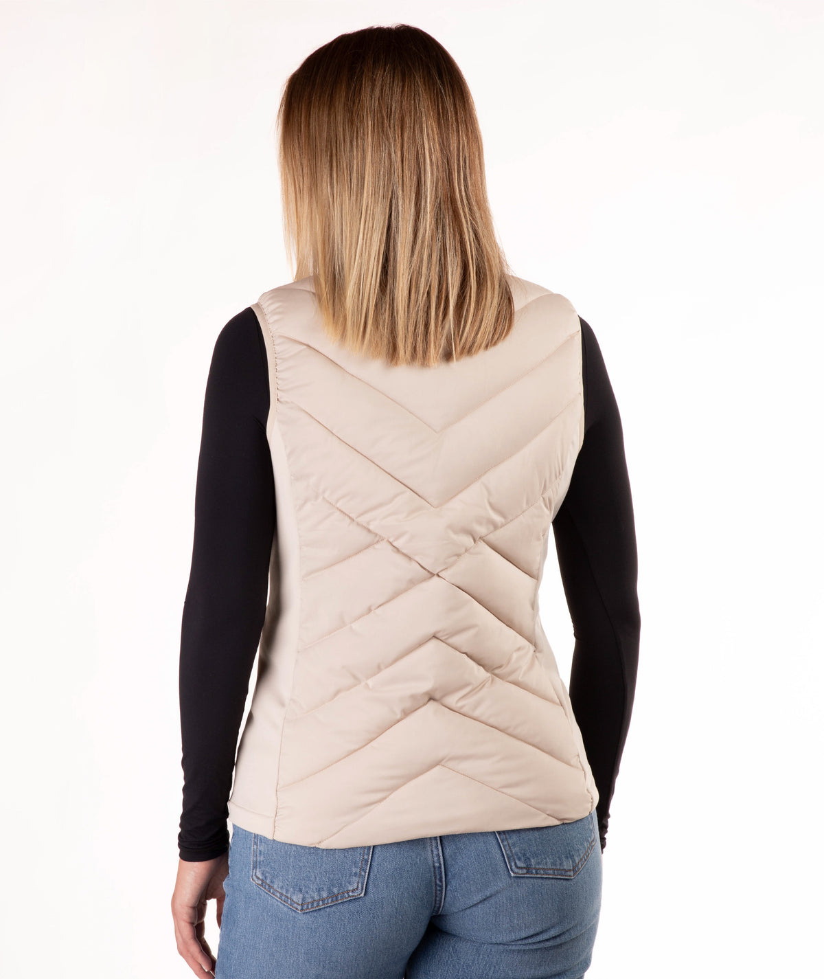 A woman viewed from the back wearing a light beige quilted puffer vest over a black long-sleeve top and blue jeans, against a plain white background.