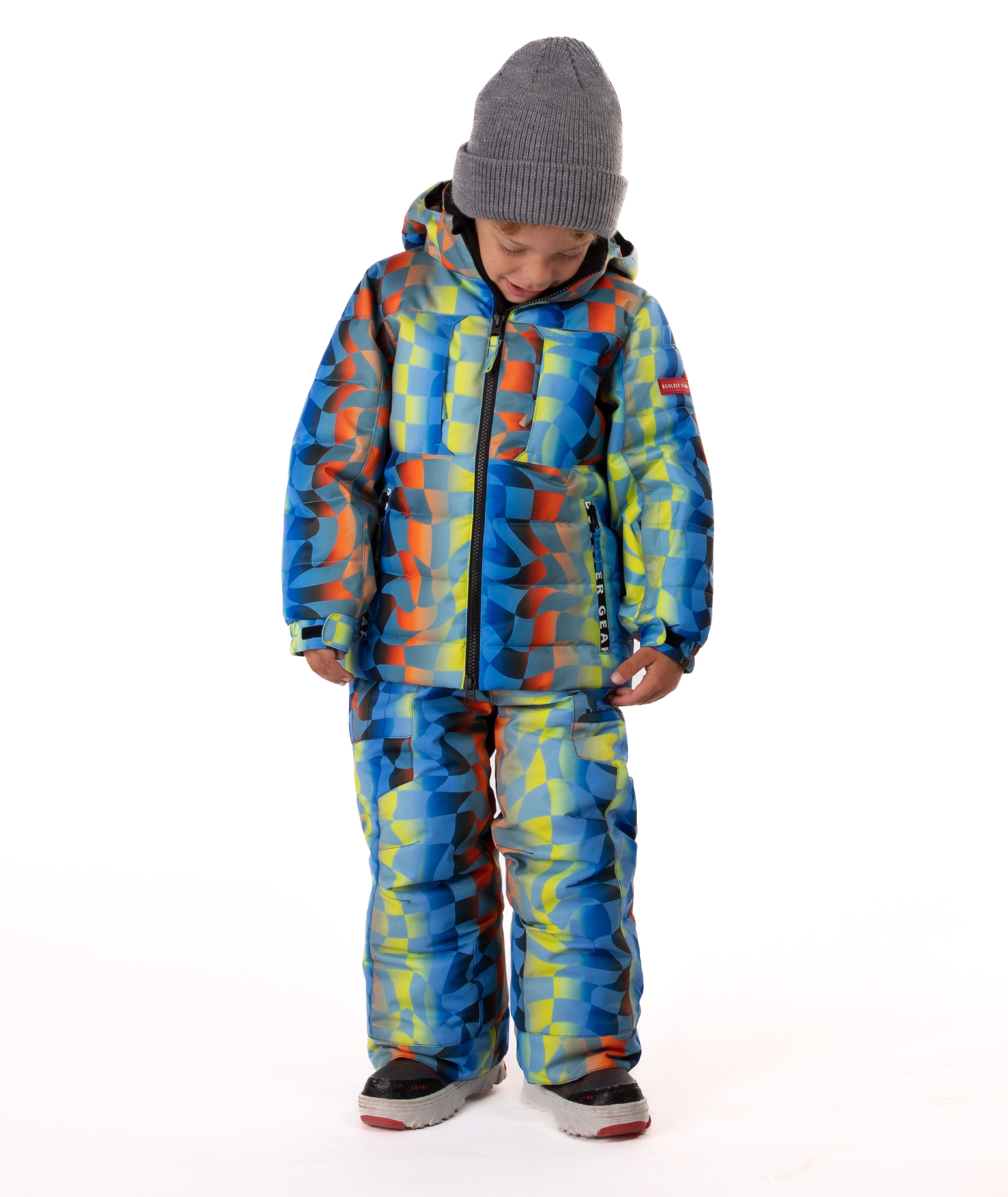 Child wearing a yellow, blue, and orange multi color geometric print quilted winter jacket with chest pockets and hand-warmer pockets on a white background
