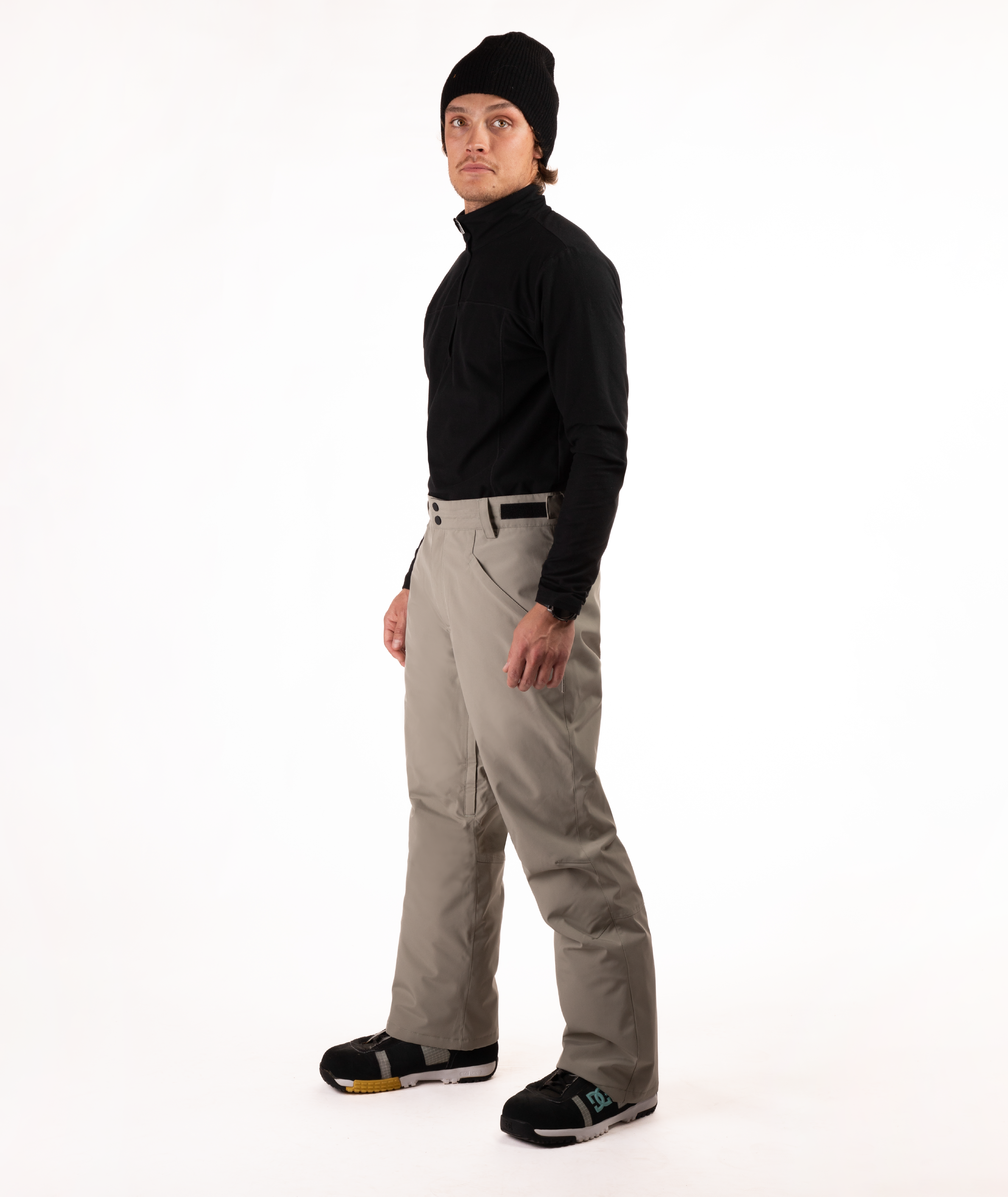 Person wearing a black top and beige snow pants on a white background