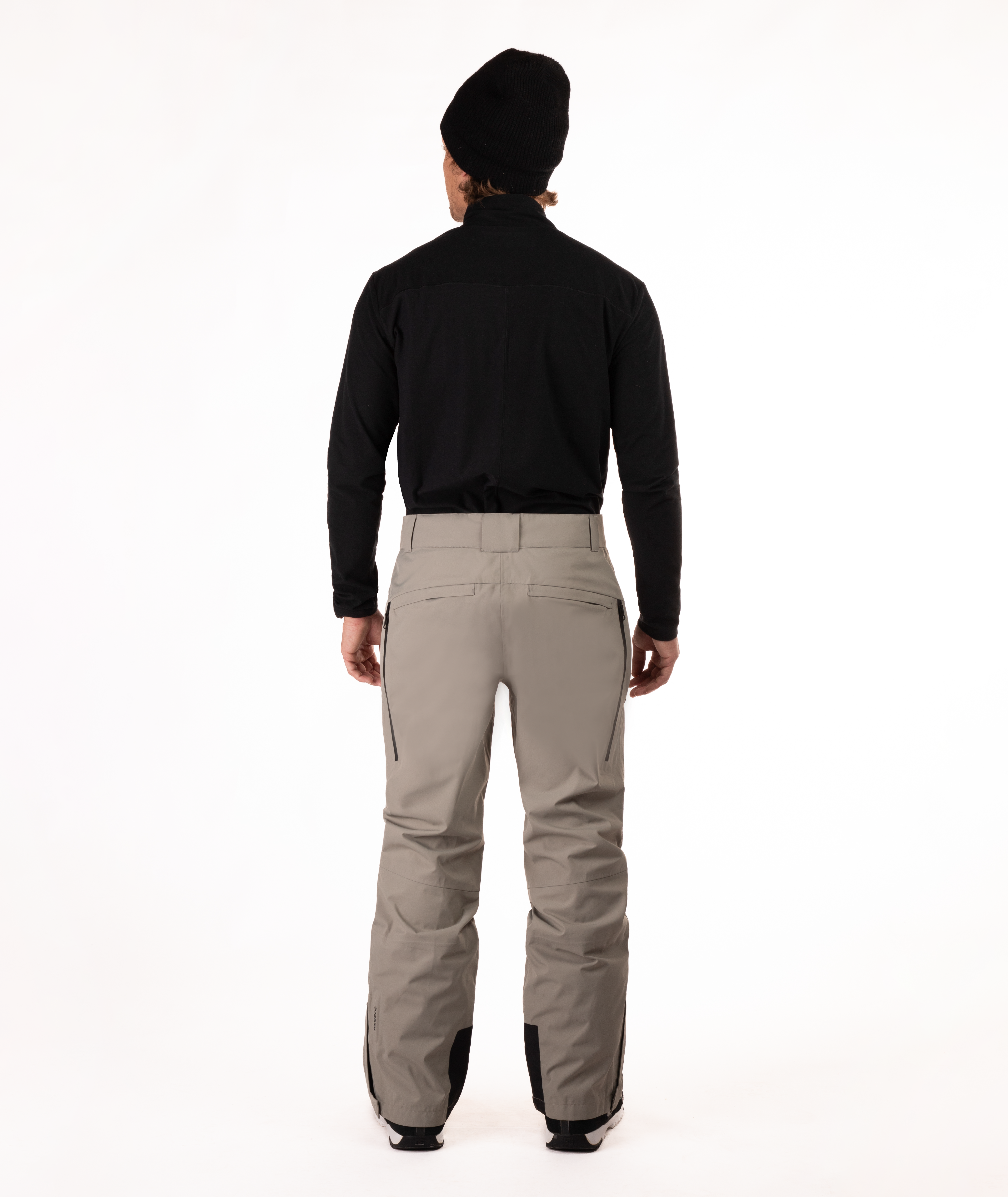 back of a person wearing a black top and beige snow pants on a white background