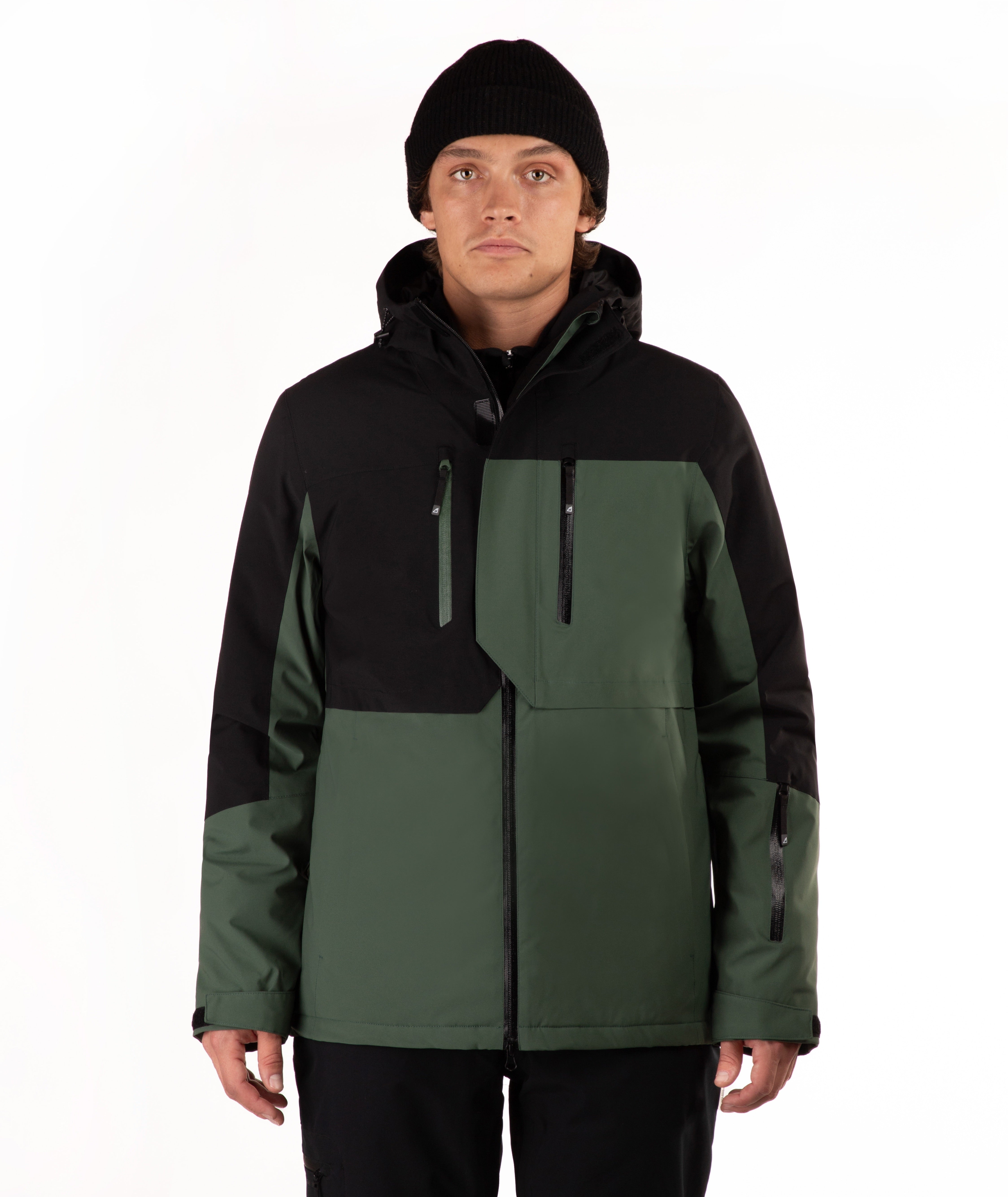 A man wearing a black and dark green color-blocked ski jacket, a black beanie, and black pants, standing against a plain white studio background.