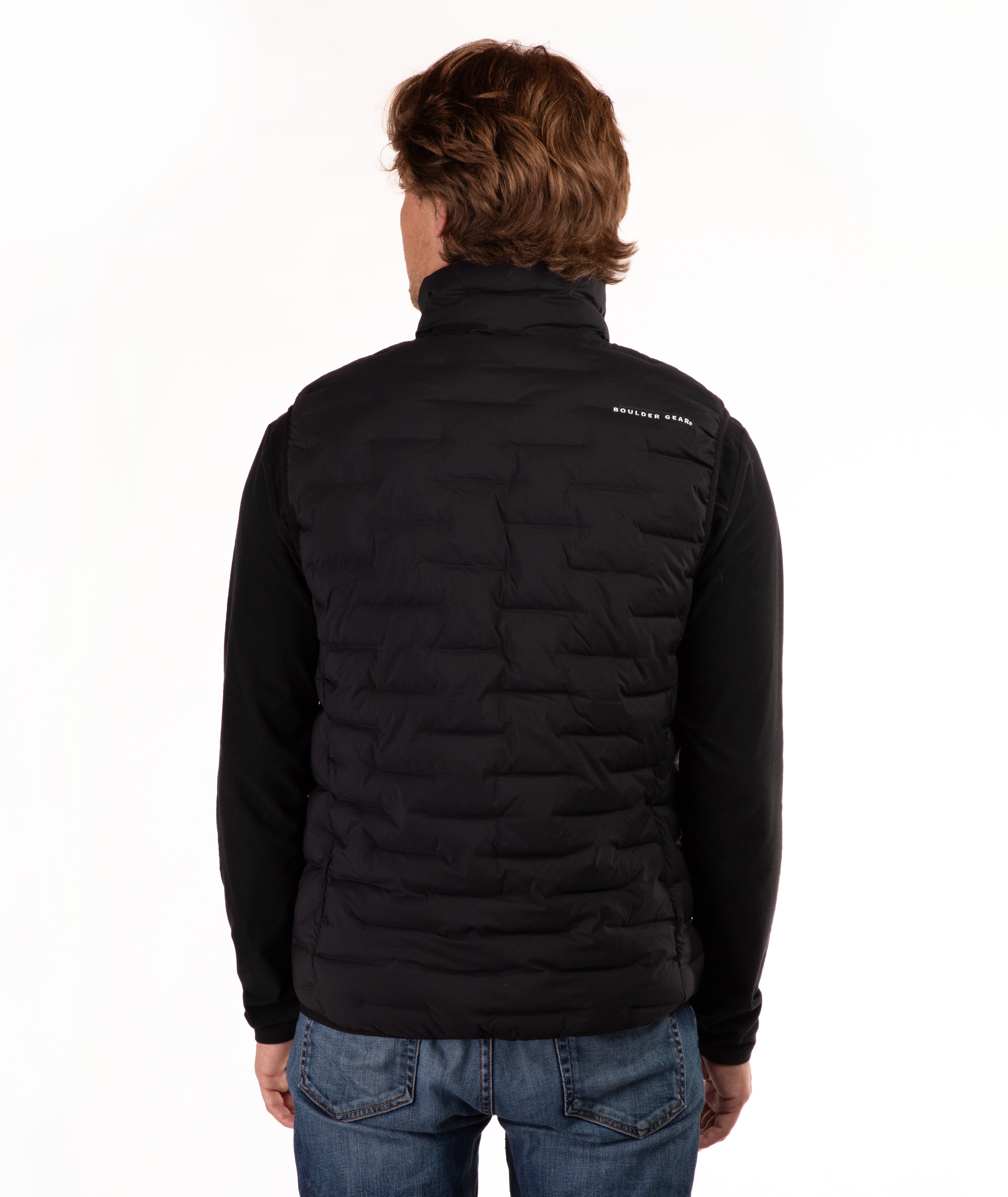 A man viewed from the back wearing a black quilted vest over a black long-sleeve shirt and blue jeans, against a plain white background.