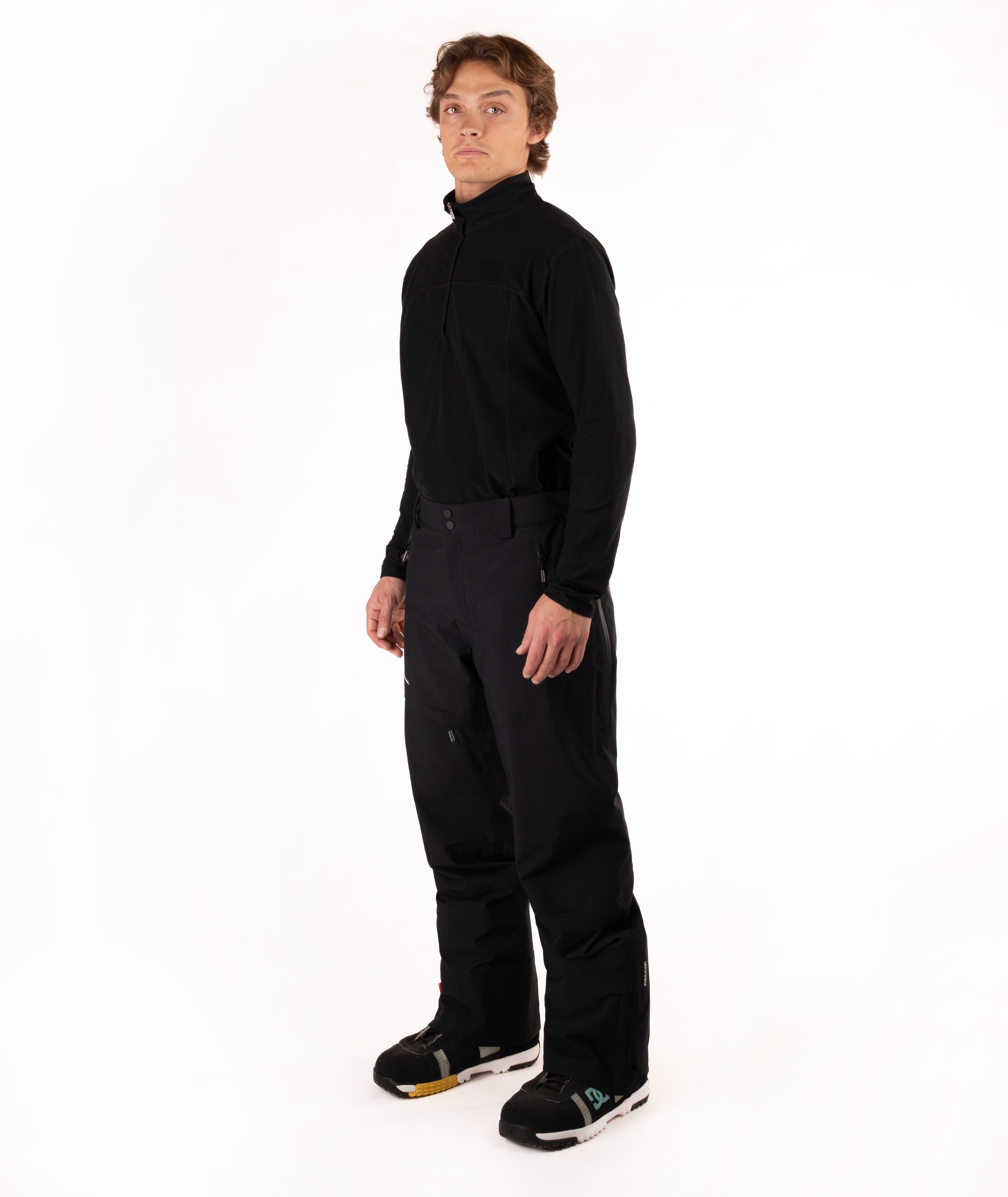 A man wearing a black long-sleeve half-zip athletic top and black ski pants, standing against a solid white studio background.