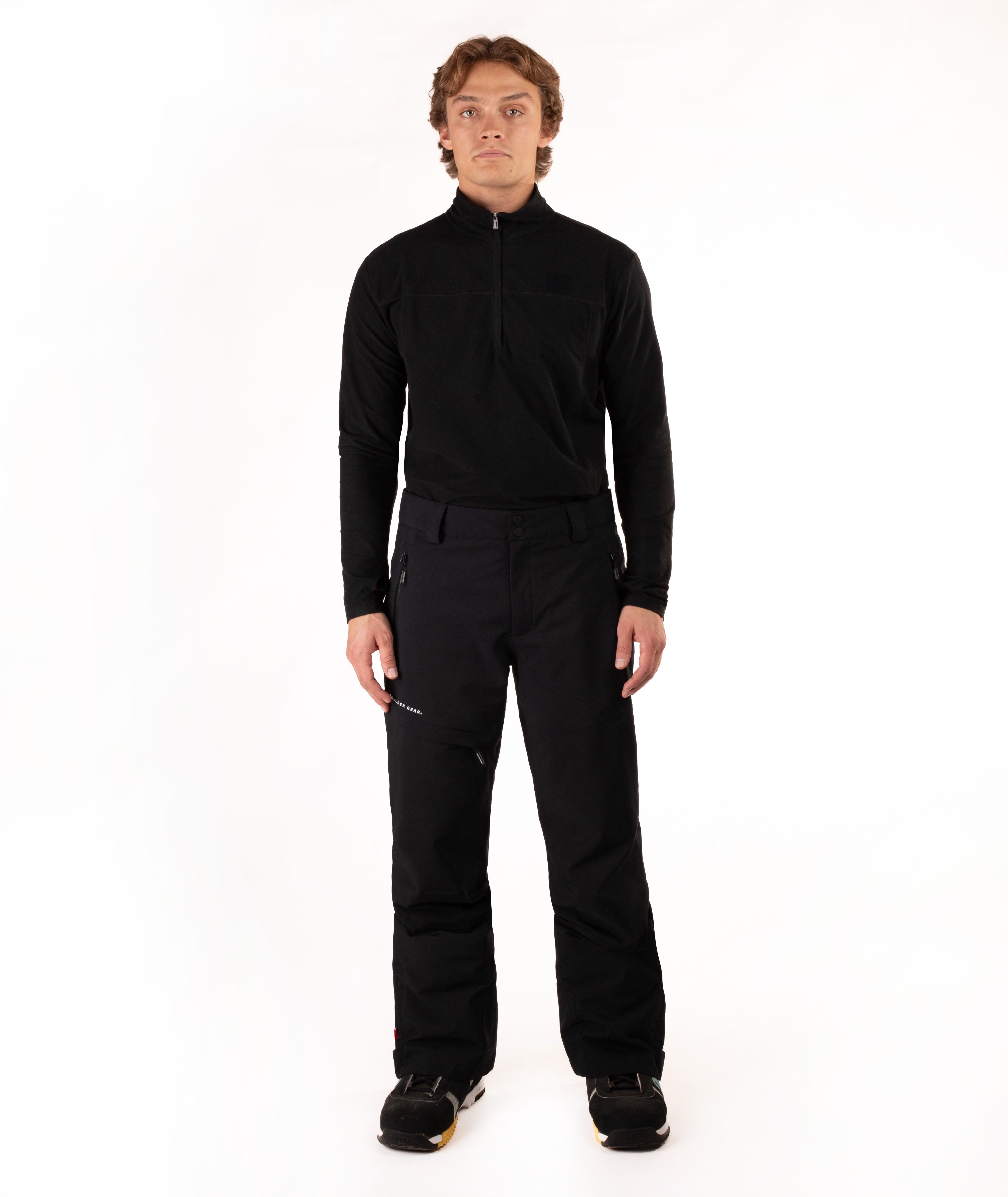 A man wearing a black long-sleeve half-zip athletic top and black ski pants, standing against a solid white studio background.
