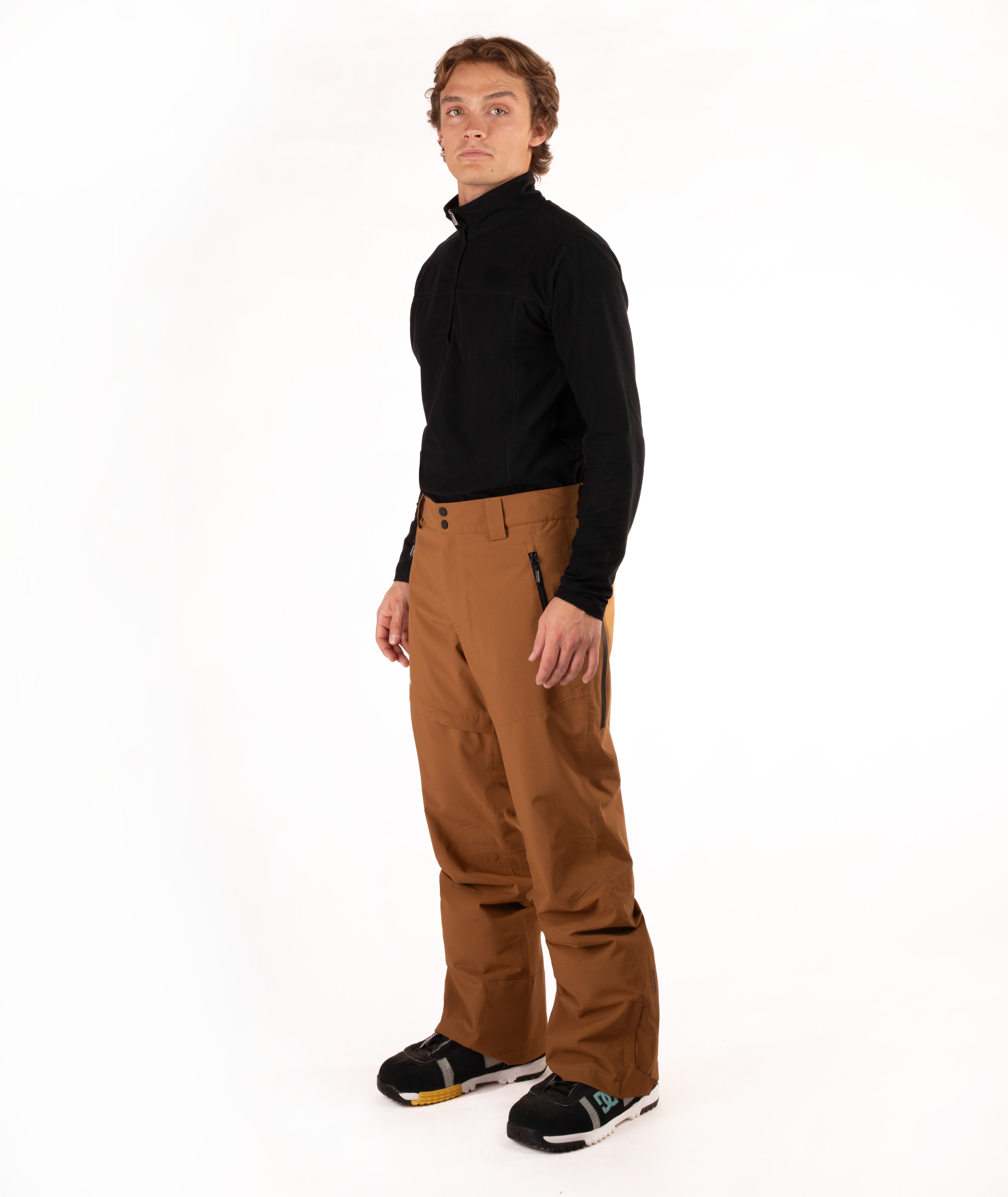 A man modeling a black long-sleeve quarter-zip fleece and brown ski pants against a solid white studio background.