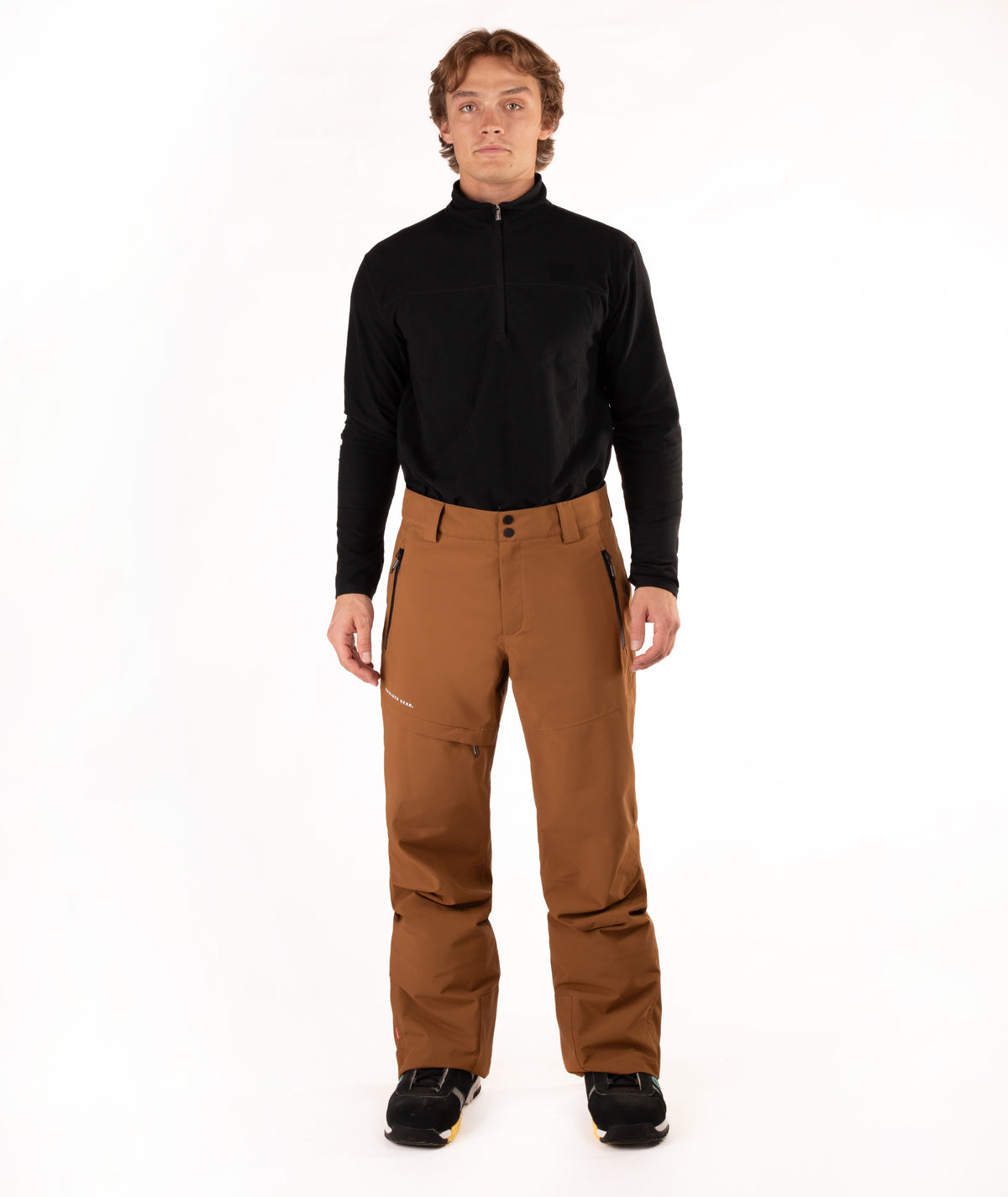 A man modeling a black long-sleeve quarter-zip fleece and brown ski pants against a solid white studio background.