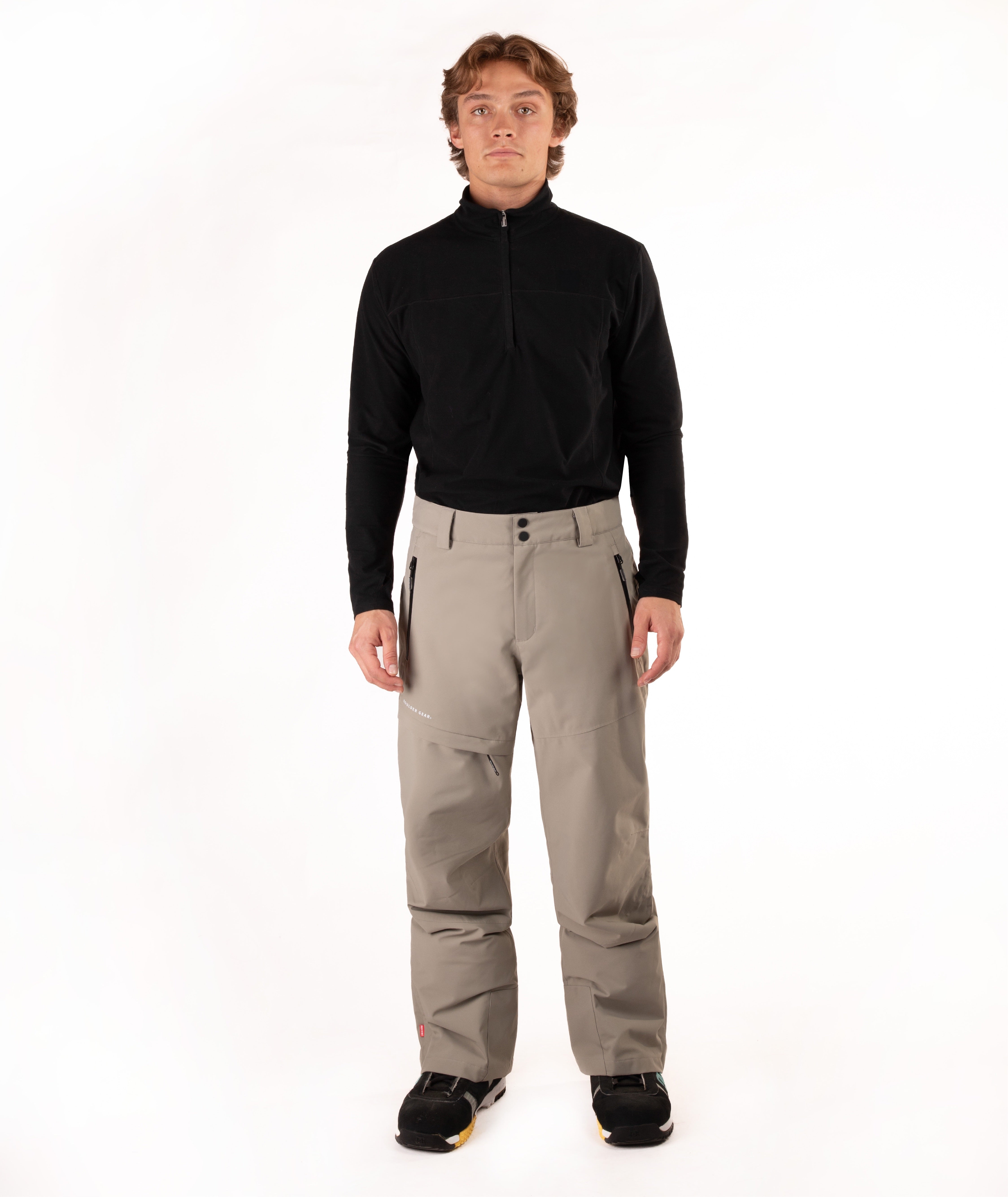 A man modeling a black long-sleeve quarter-zip fleece and beige ski pants against a white studio background.
