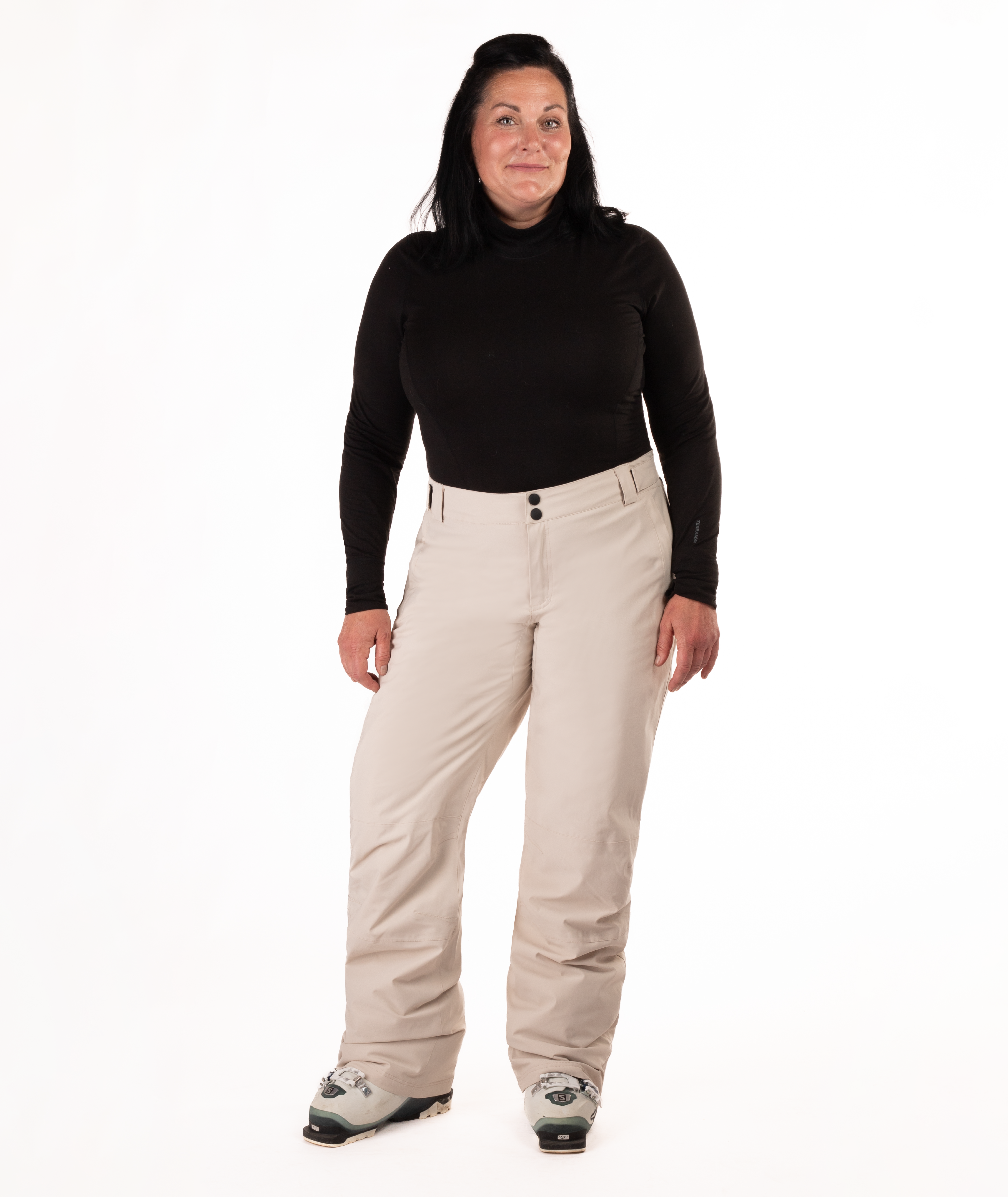 Person wearing a black long-sleeve top and beige snow pants on a white background