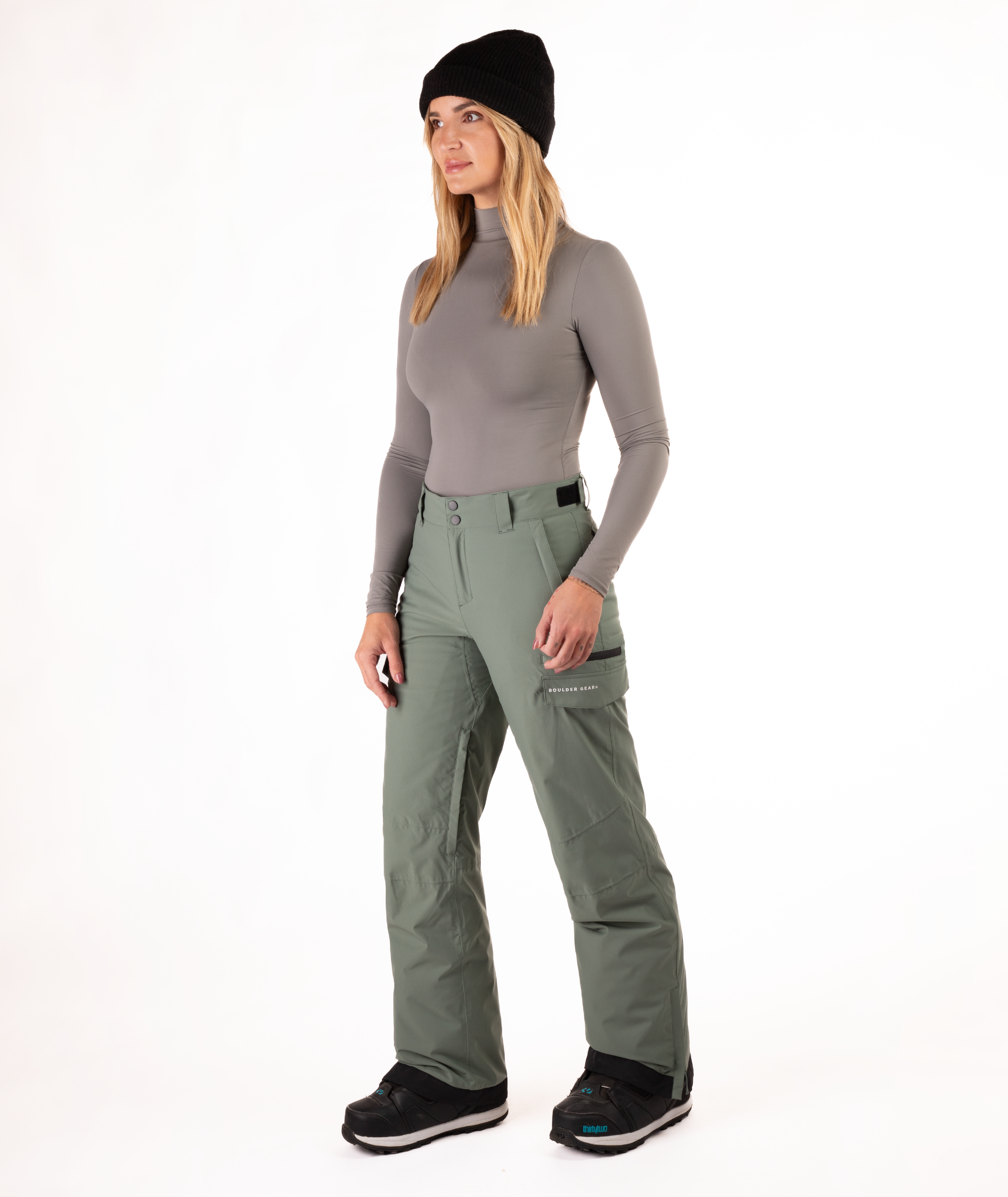 Person wearing a gray long-sleeve top and green snow pants on a white background