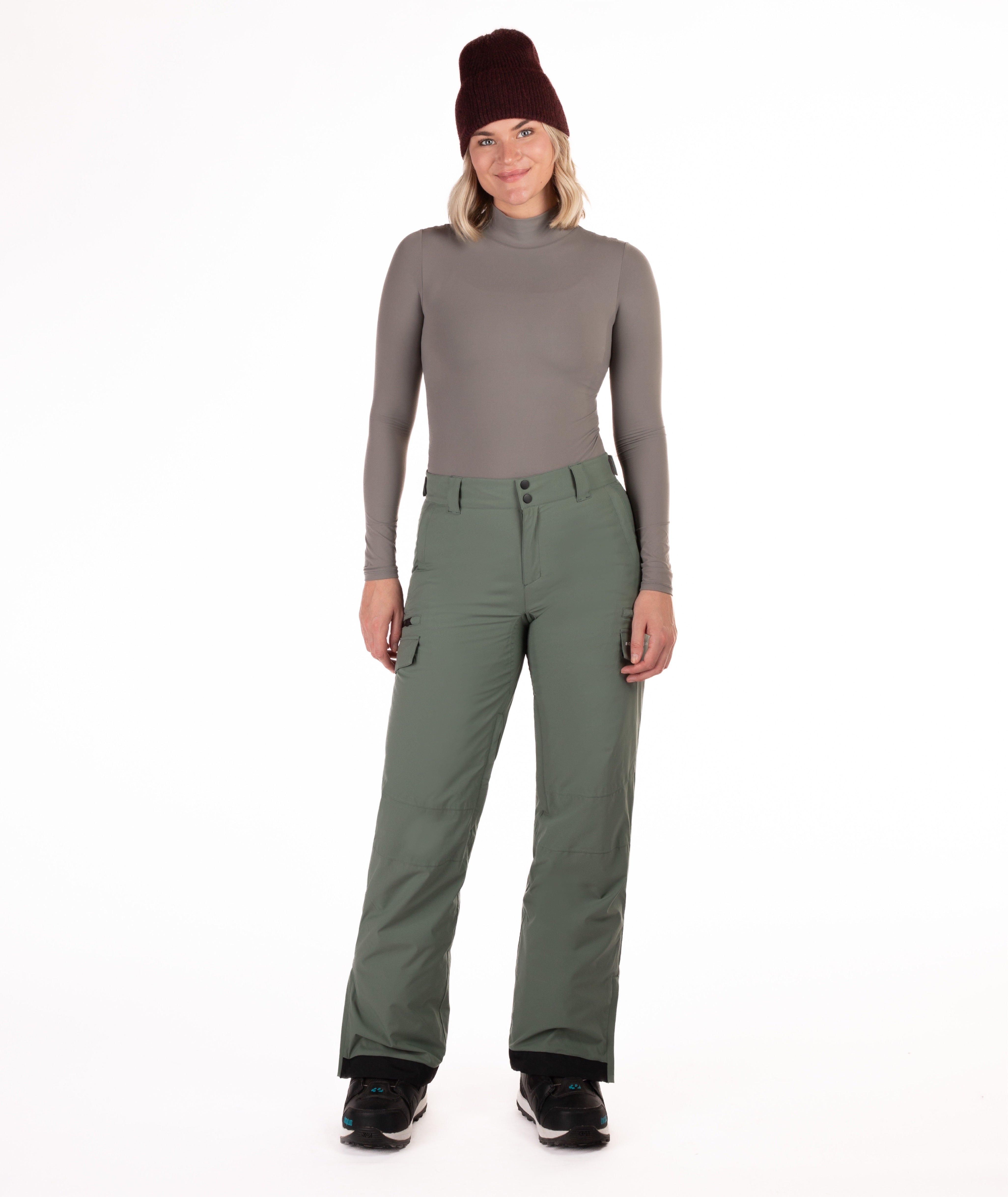 Person wearing a gray long-sleeve top and green snow pants on a white background