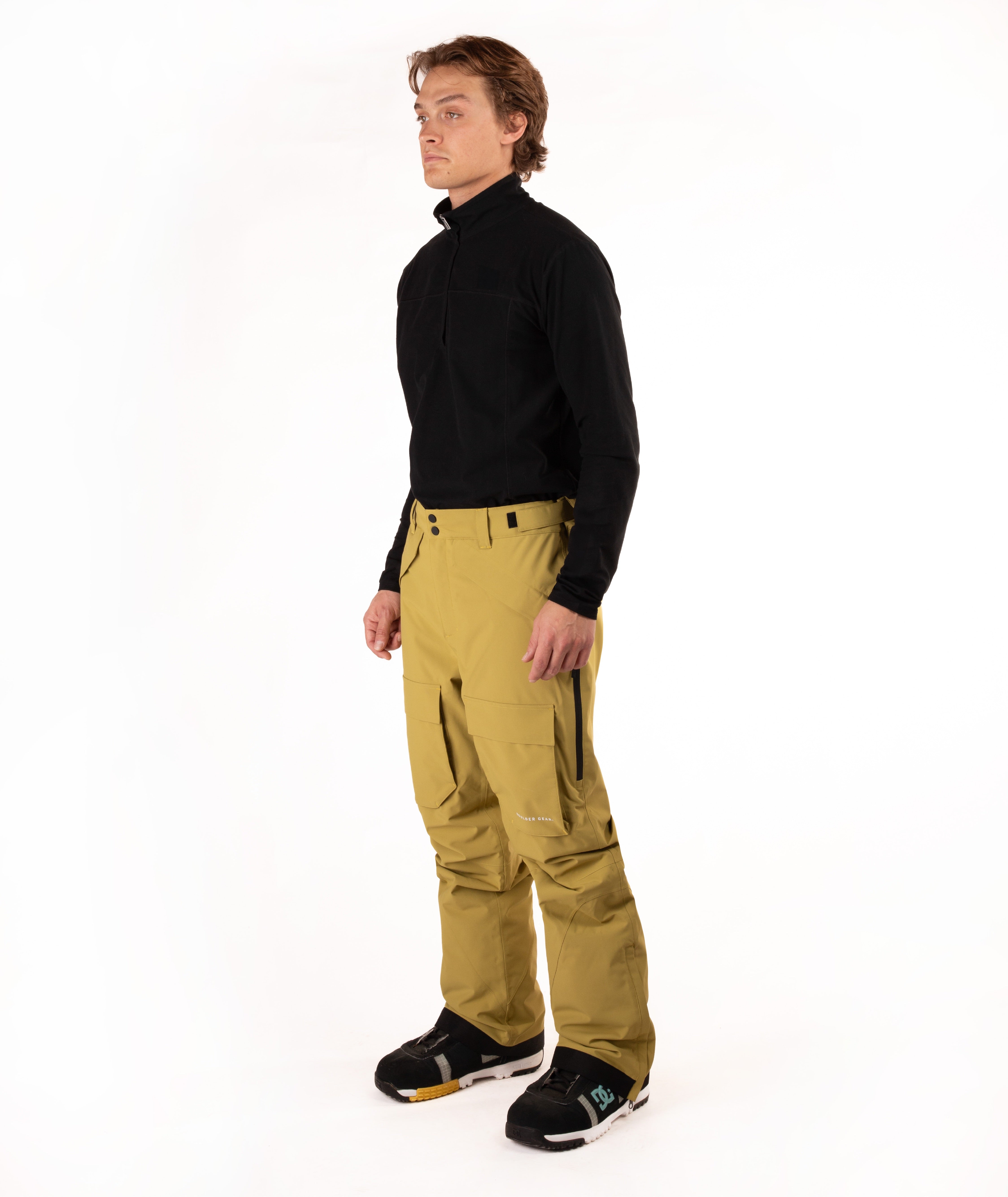 A man modeling a black long-sleeve quarter-zip fleece and mustard yellow snow pants with black snow boots, standing against a solid white studio background.