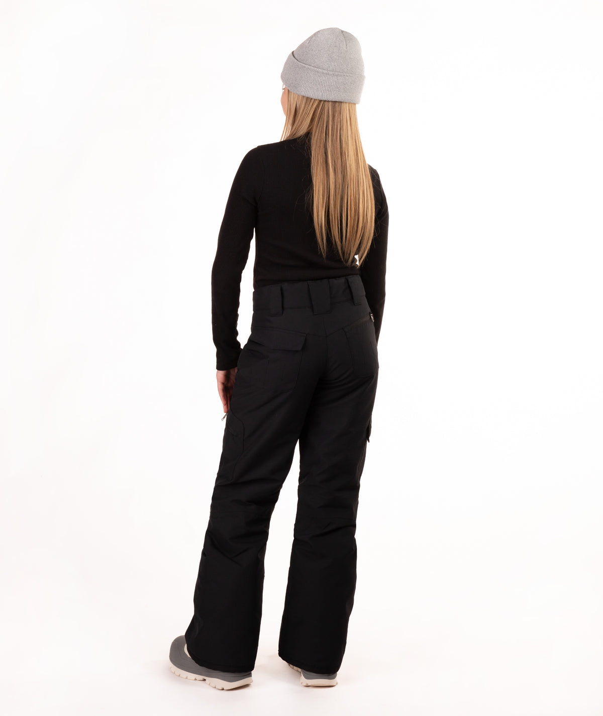 A girl shown from the back wearing a light gray beanie, a black long-sleeve top, black pants, and gray sneakers, standing against a plain white studio background.