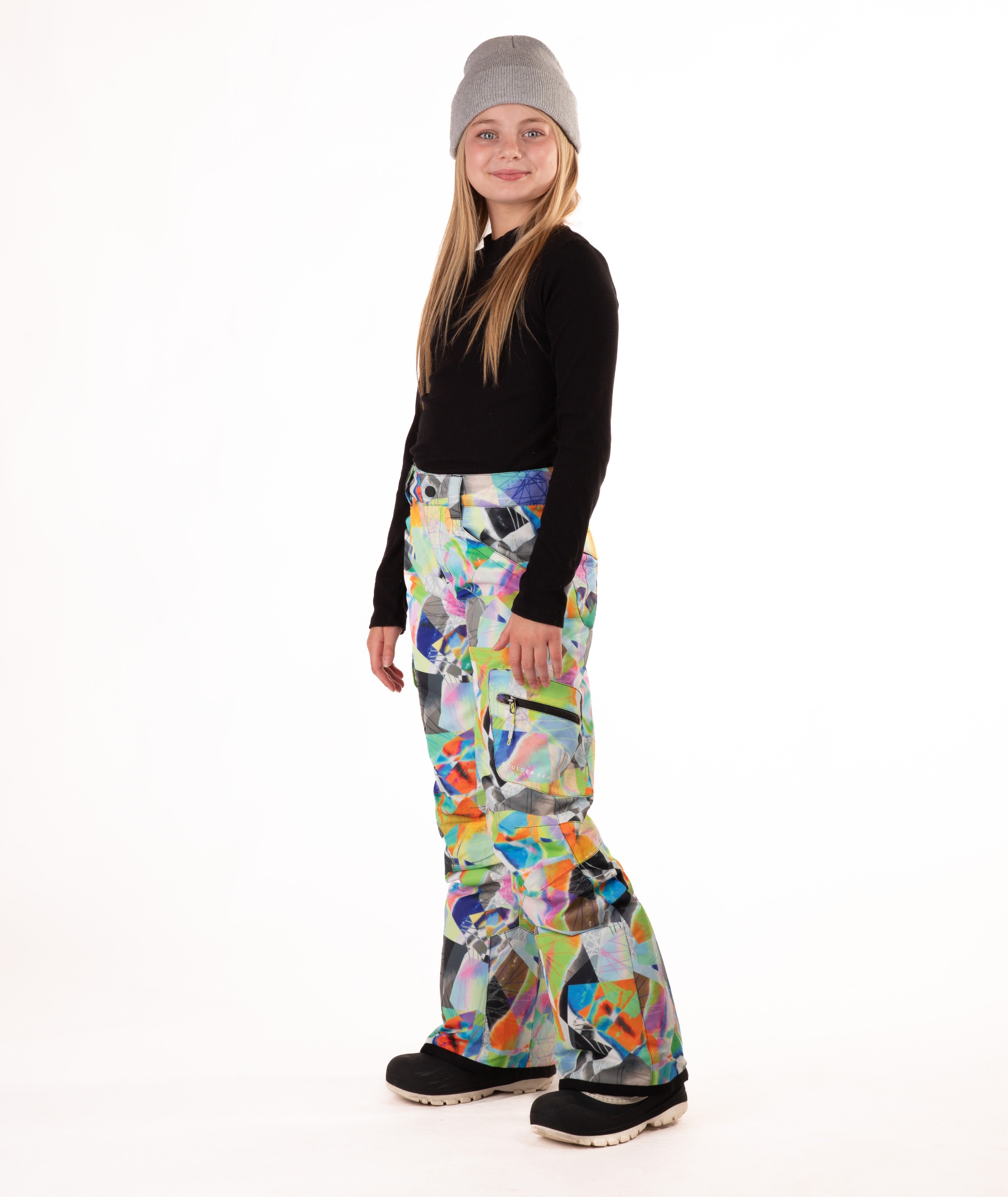 Girl wearing multi colored geometric patterned snow pants and a black top on a white background