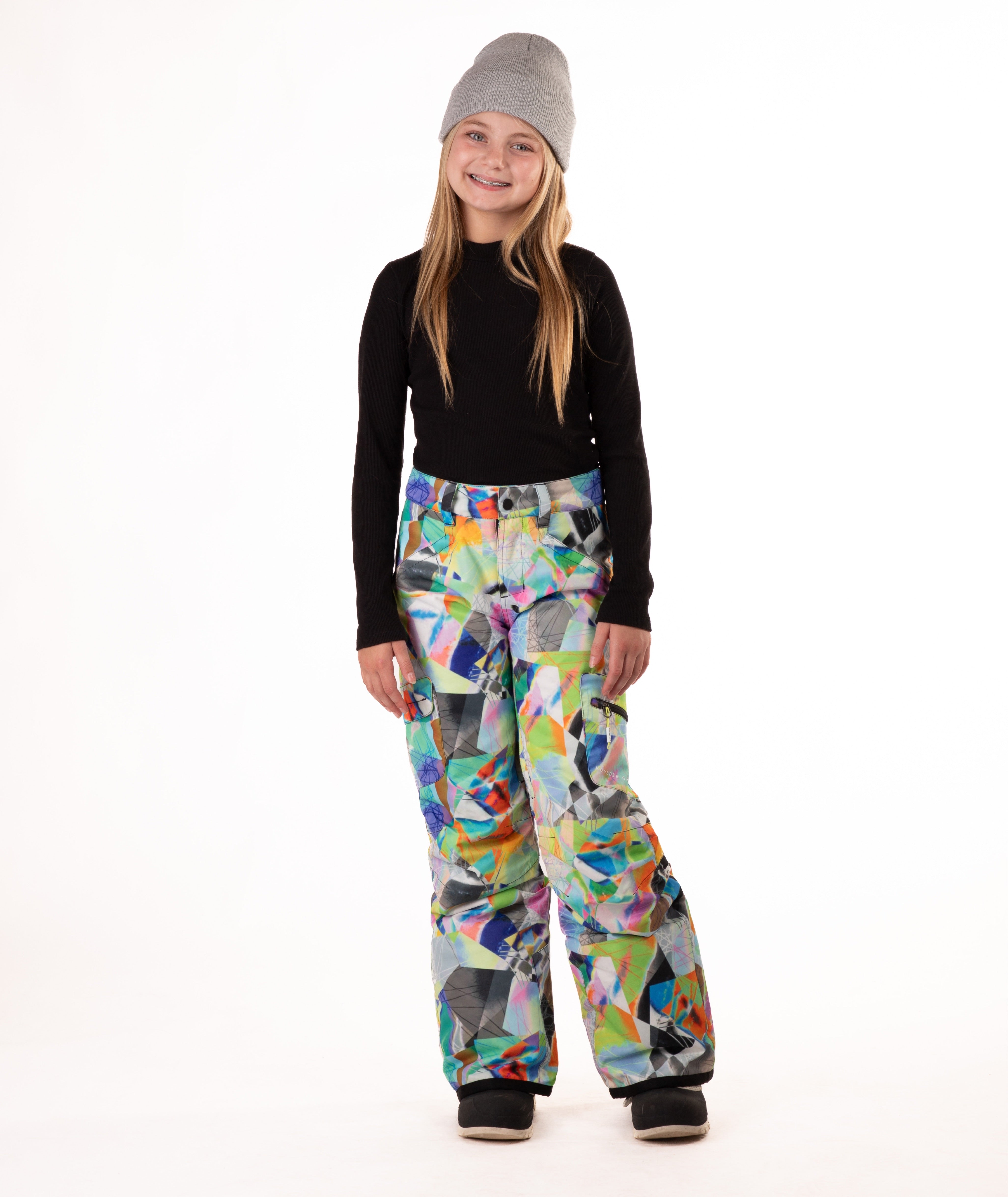 Girl wearing multi colored geometric patterned snow pants and a black top on a white background
