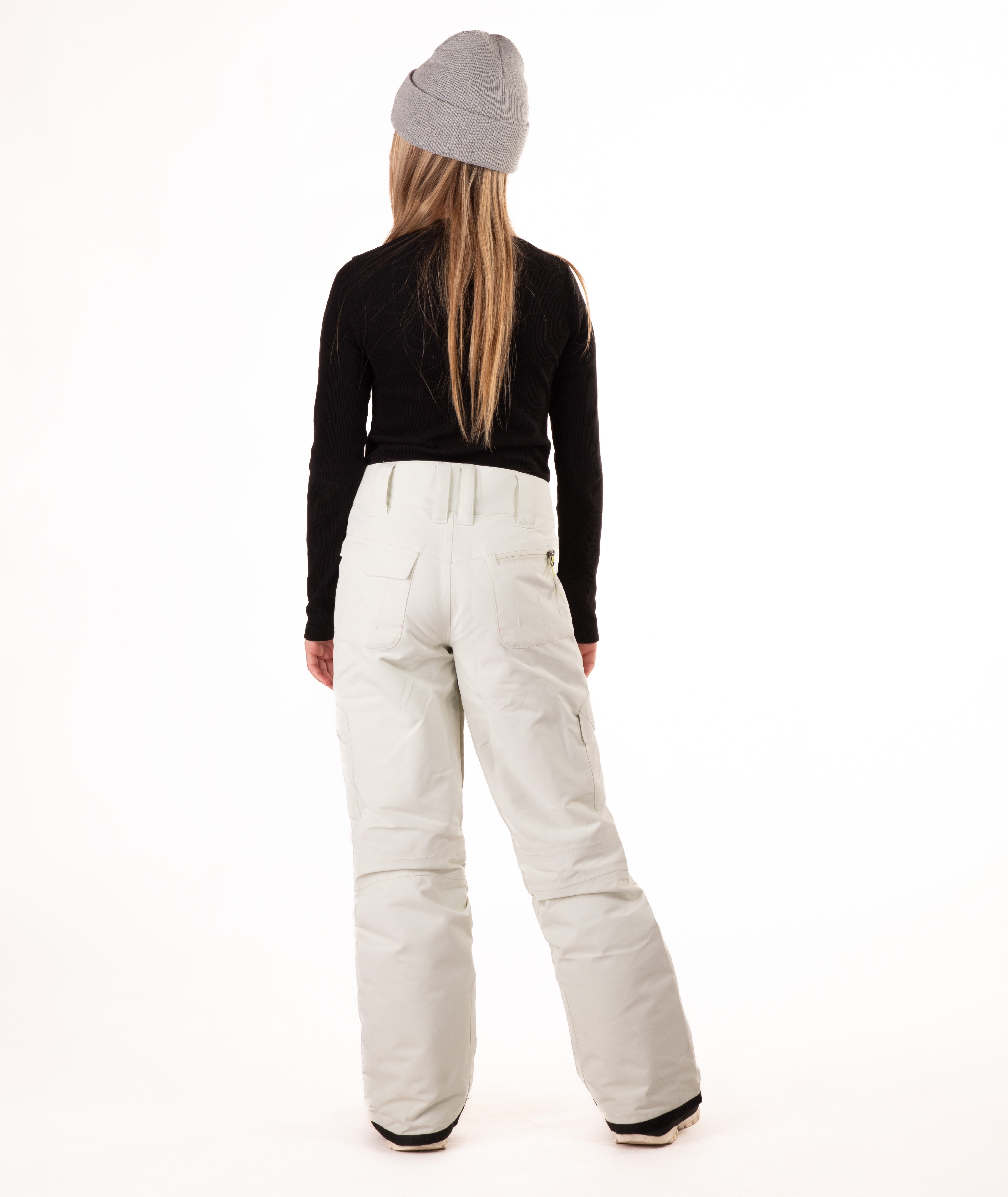 back of a girl wearing cream colored snow pants and a black long-sleeve top on a white background