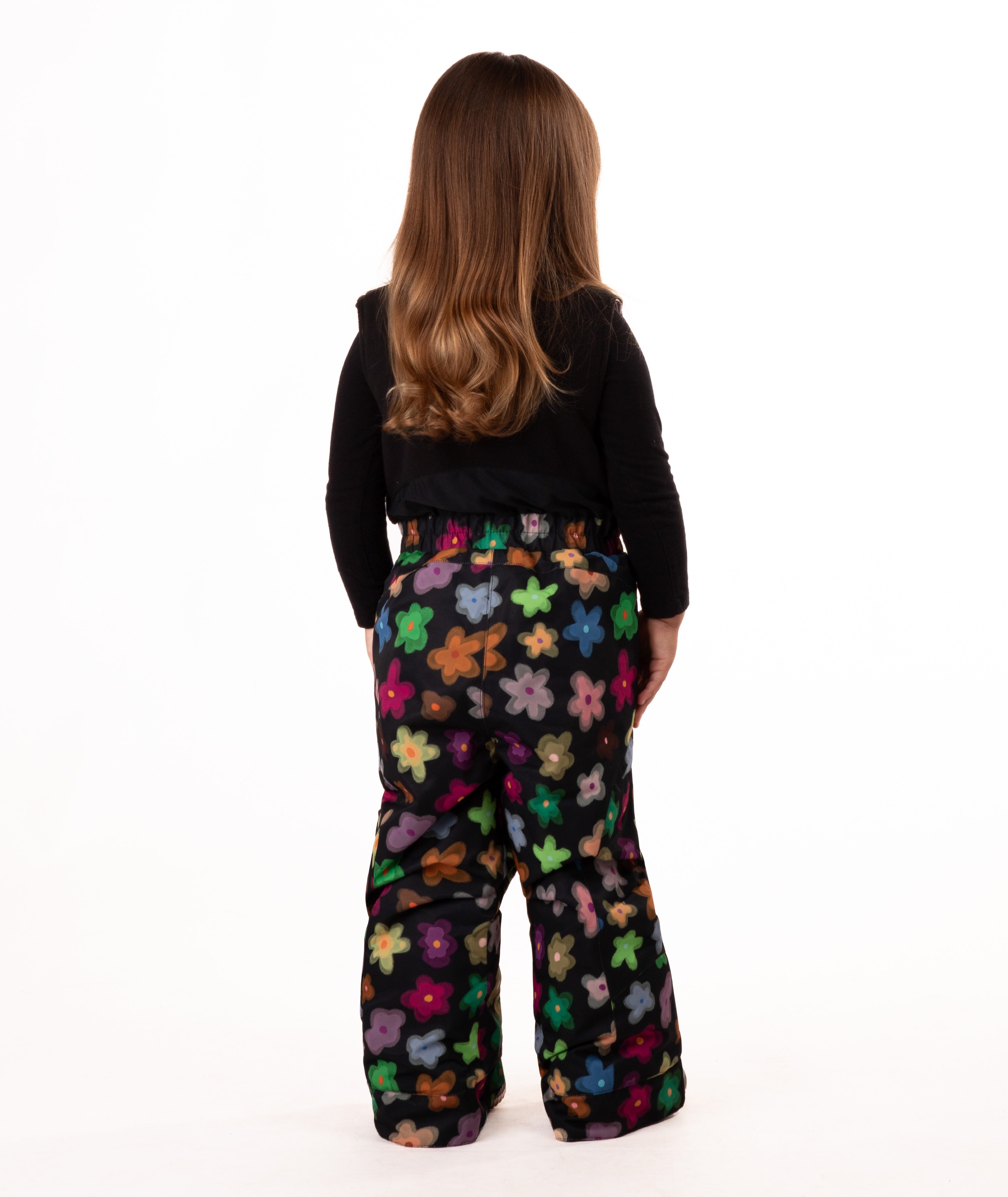 back of child wearing a multi color flower print snow bib with black top on a white background