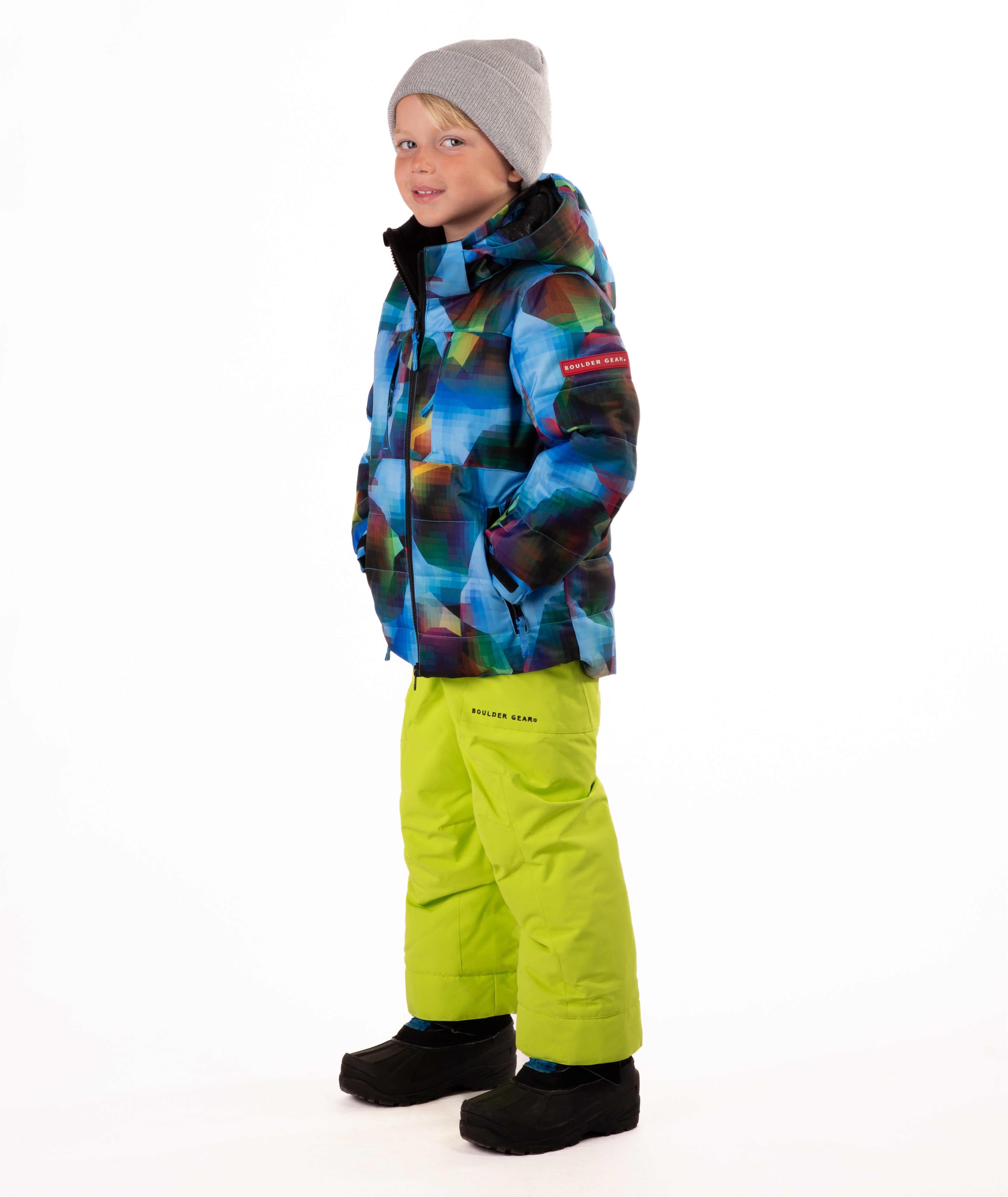 Child wearing a yellow, blue, and black multi color print quilted winter jacket with chest pockets and hand-warmer pockets on a white background highlighting a red Boulder Gear brand patch on the left sleeve