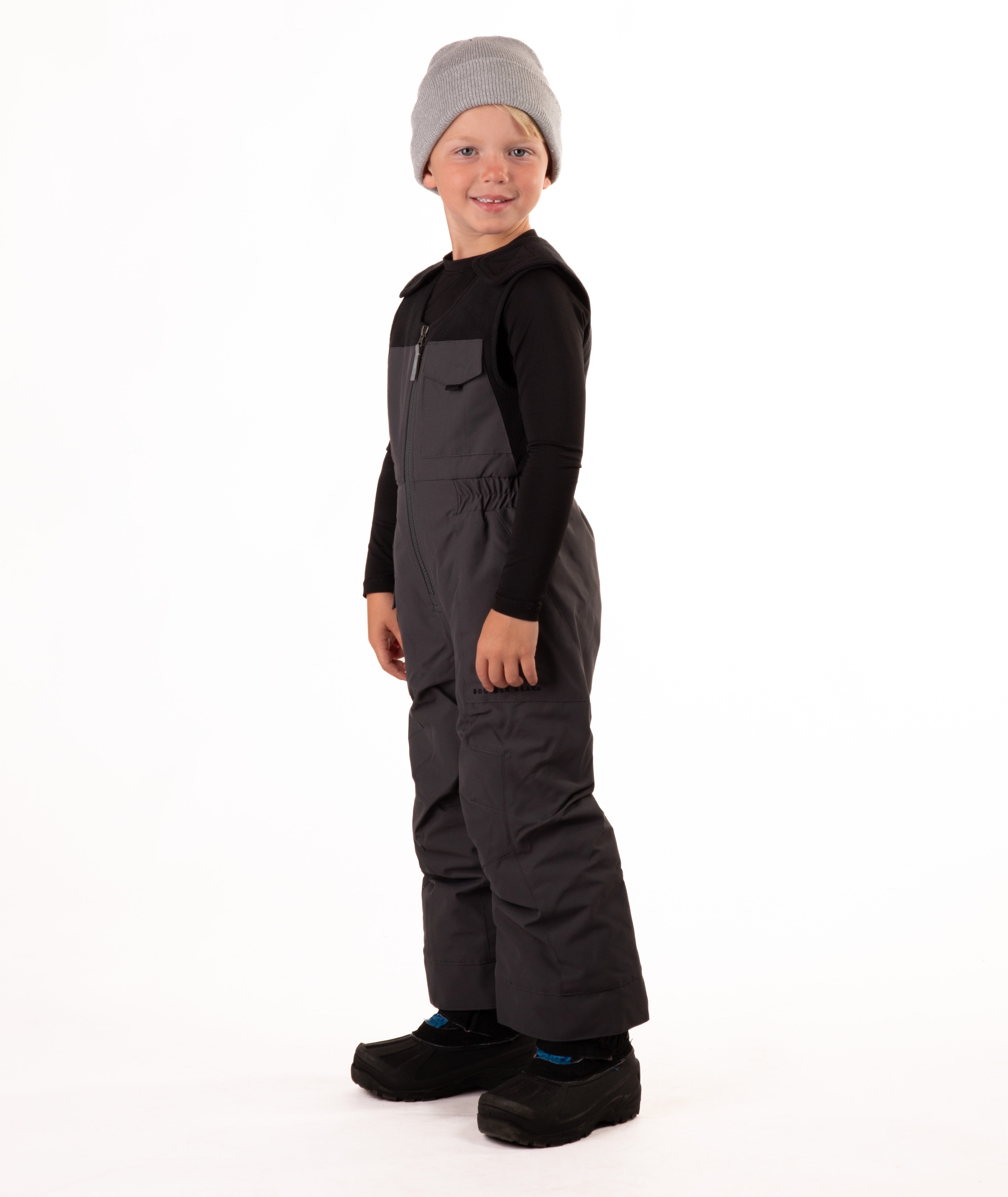 Child wearing dark gray snow bibs on a white background