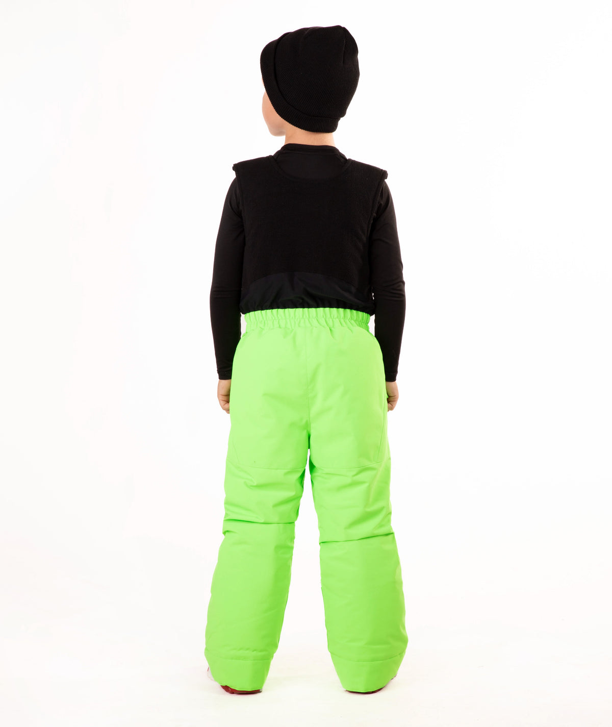 A child wearing bright neon green snow bib overalls over a black long-sleeve shirt and black beanie, standing against a plain white studio background.