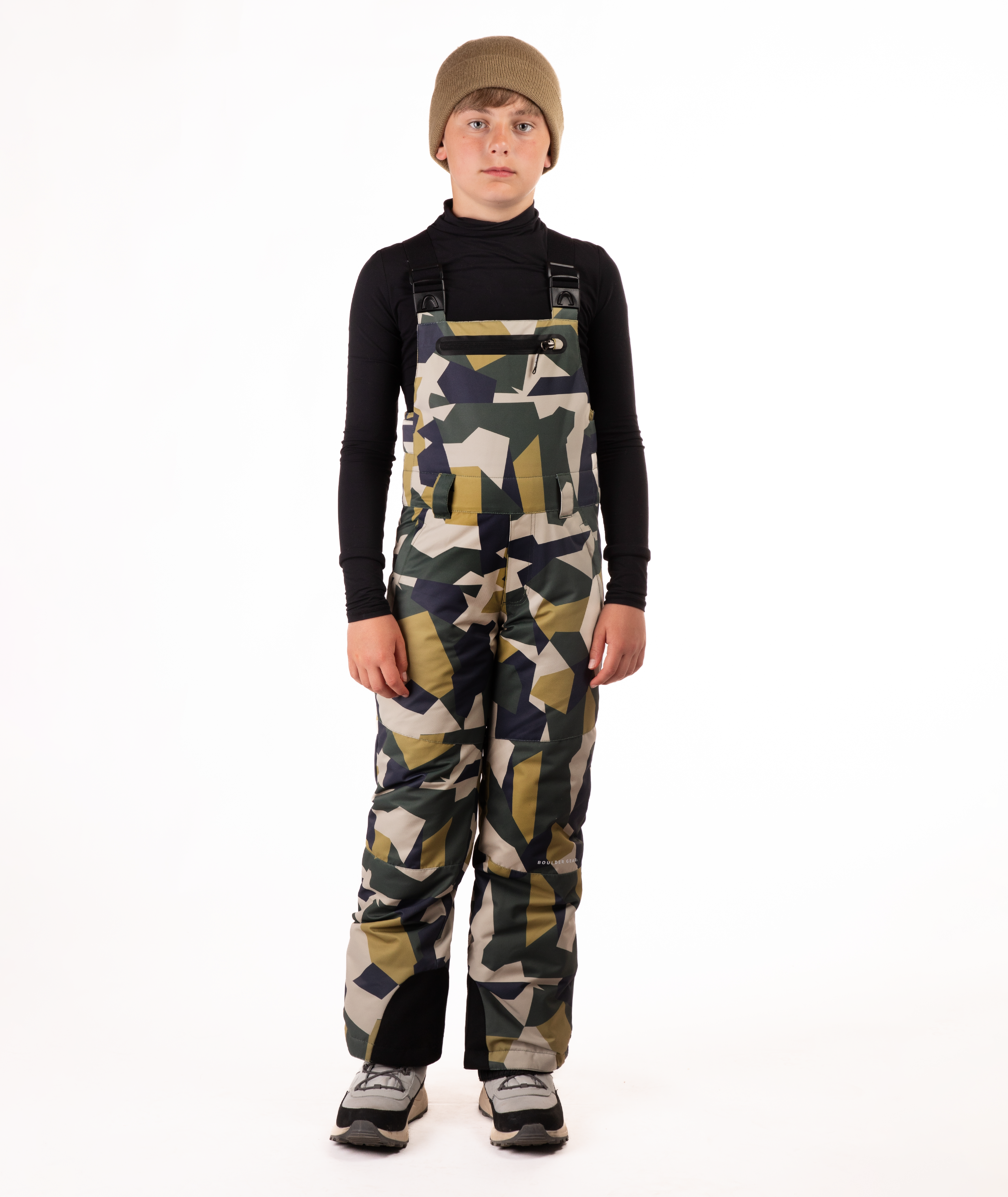 boy wearing camouflage bibs and black top on a white background