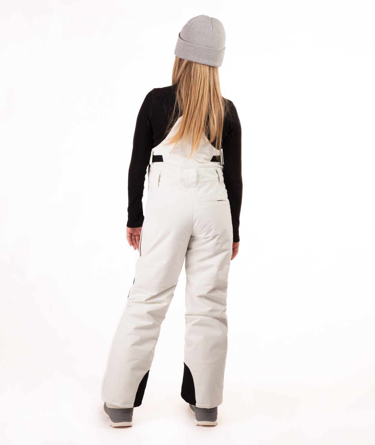 A model shown from the back wearing off-white insulated bibs with black contrast panels at the lower legs, a black long-sleeve top, and a gray beanie, set against a plain white studio background.