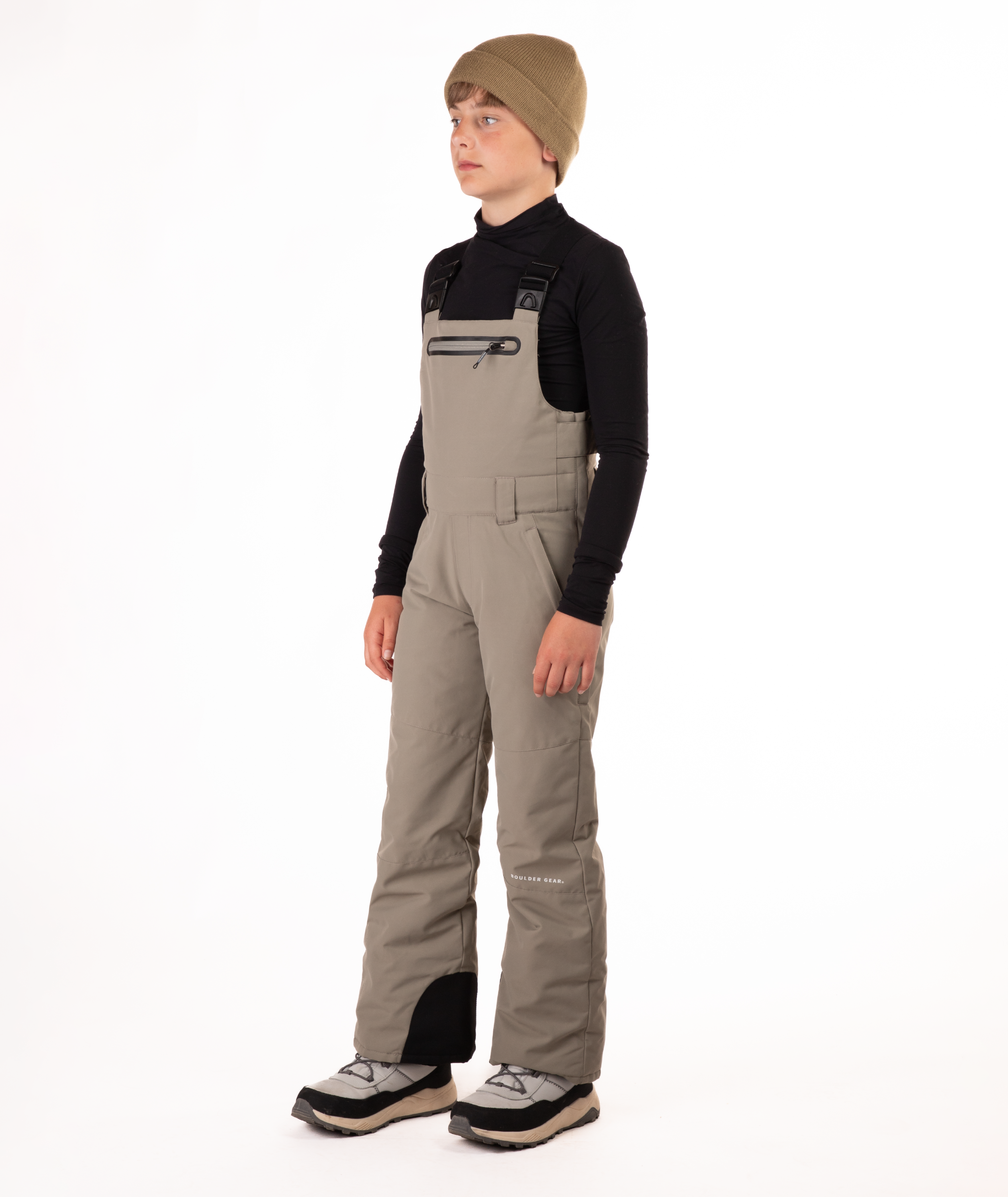 boy wearing beige bibs and black top on a white background