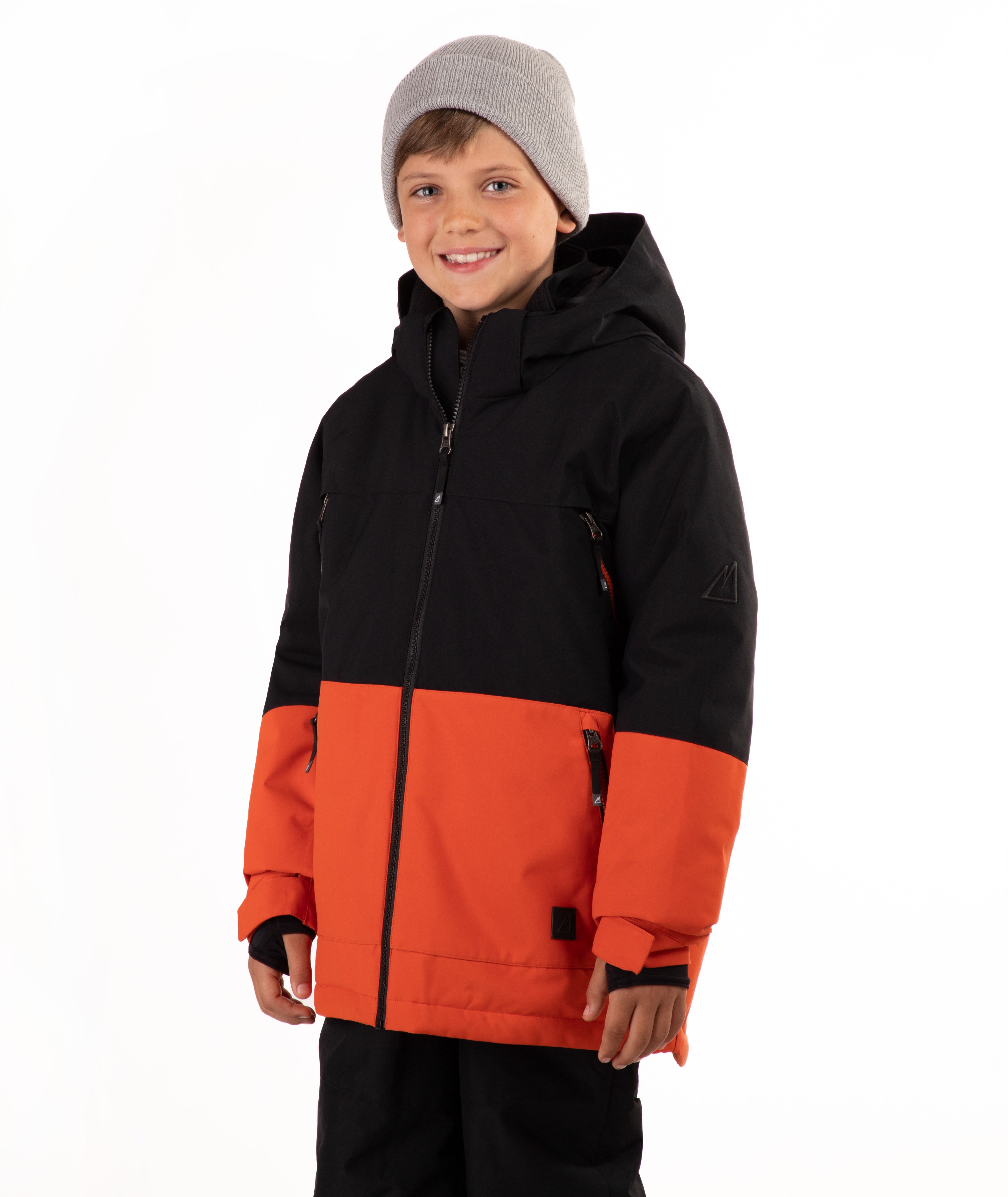 A child wearing a black and orange color-blocked hooded snow jacket, a gray knit beanie, and black pants, standing against a plain white studio background.