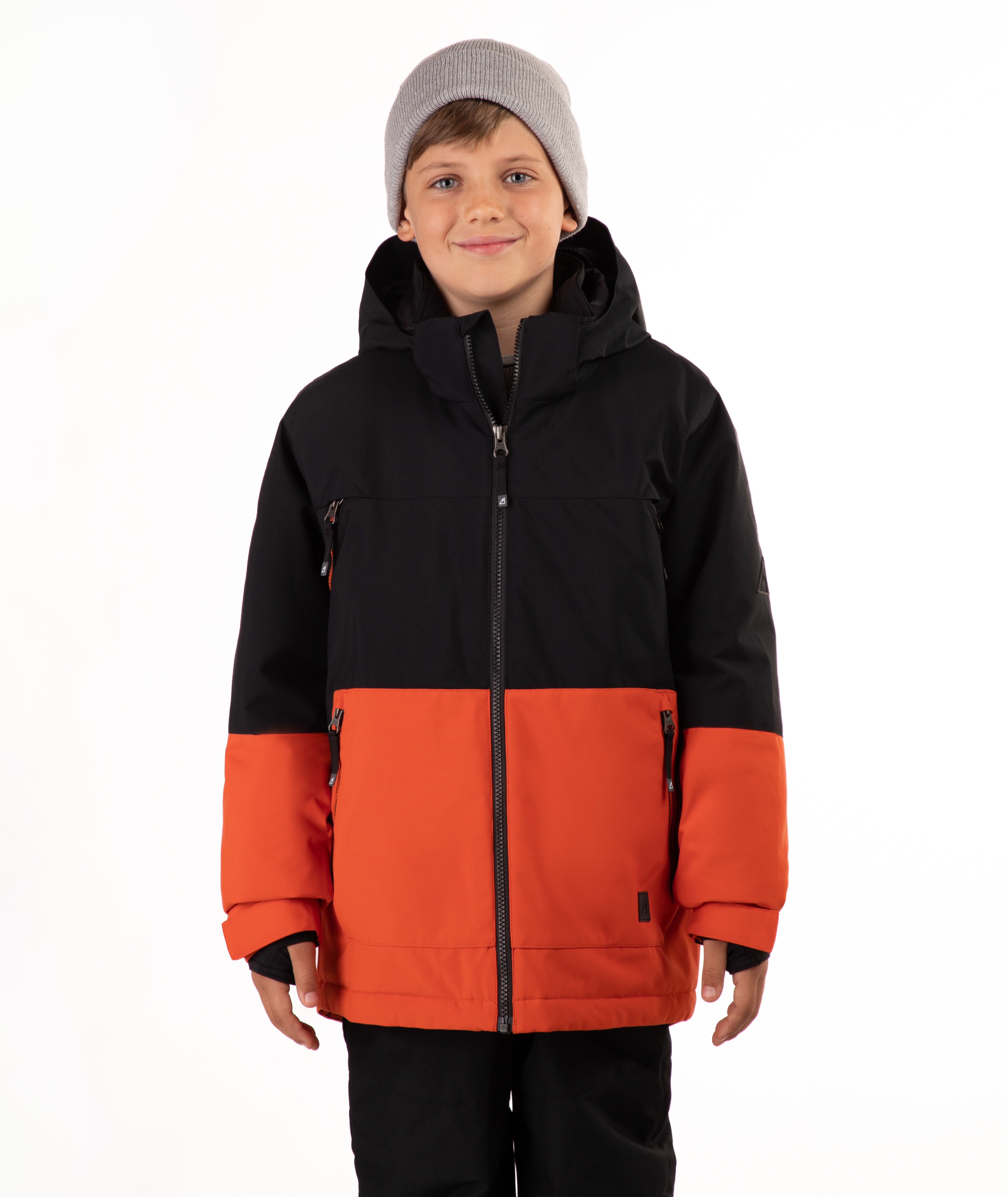 A child wearing a black and orange color-blocked hooded snow jacket, a gray knit beanie, and black pants, standing against a plain white studio background.