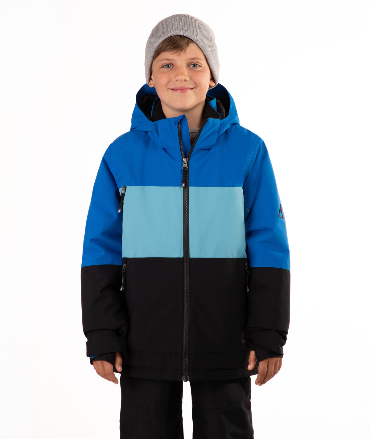 A young boy wearing a color-blocked ski jacket in blue, light blue, and black, paired with a gray beanie, standing against a plain white background.