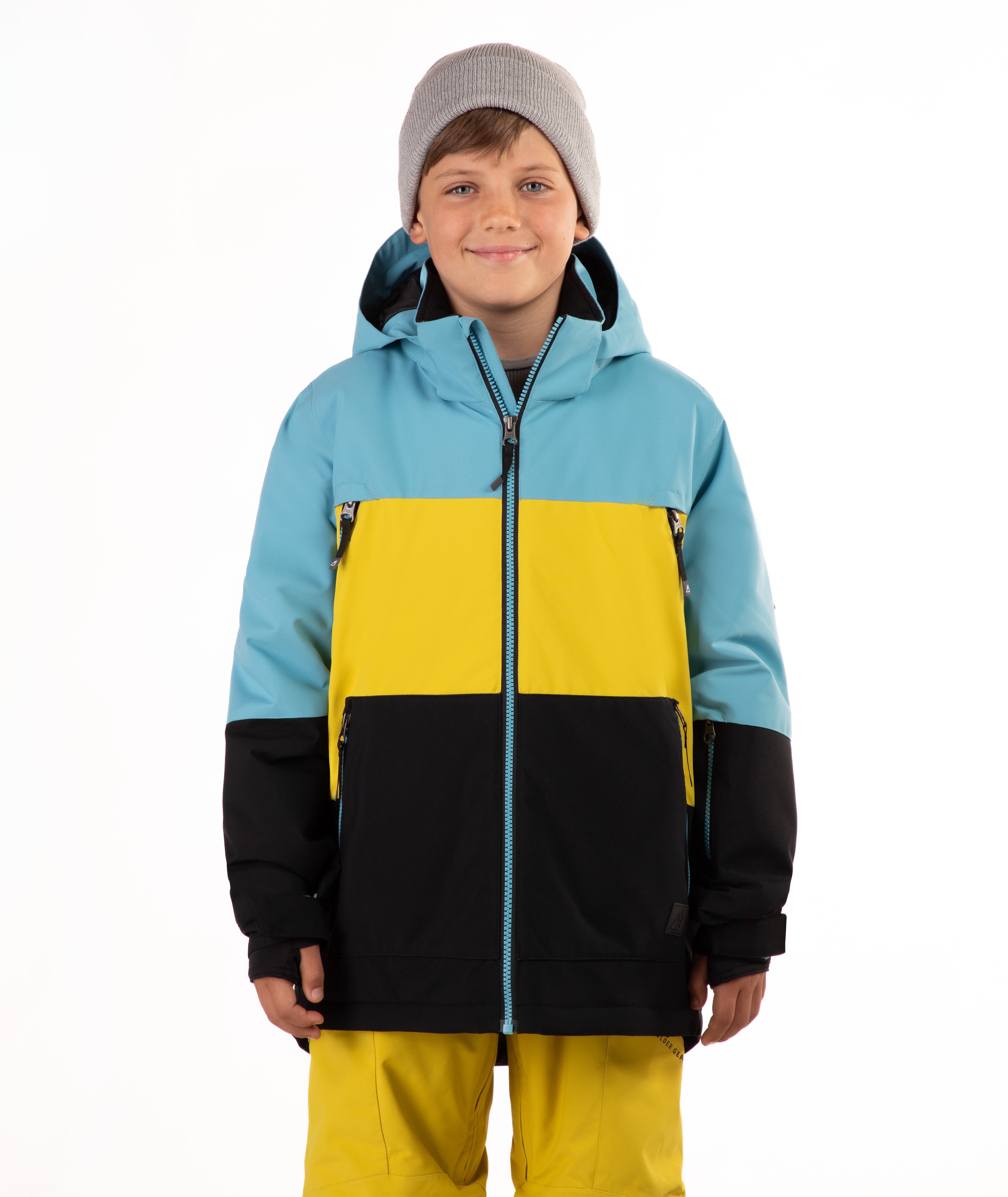 A child wearing a color-blocked ski jacket with light blue, yellow, and black panels, a gray beanie, and yellow ski pants, photographed against a plain white background.