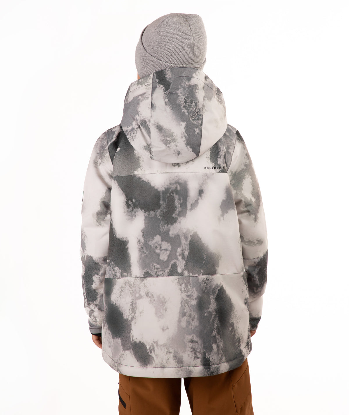 A child wearing a gray and white tie-dye patterned snowboard jacket, a gray beanie, and brown pants, standing against a plain white background.