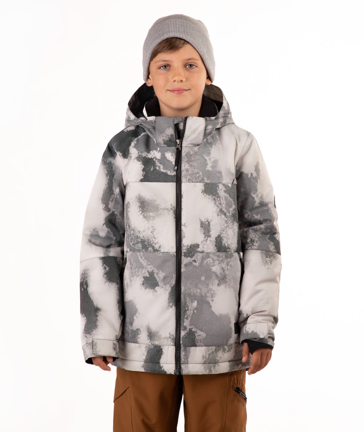 A child wearing a gray and white tie-dye patterned snowboard jacket, a gray beanie, and brown pants, standing against a plain white background.