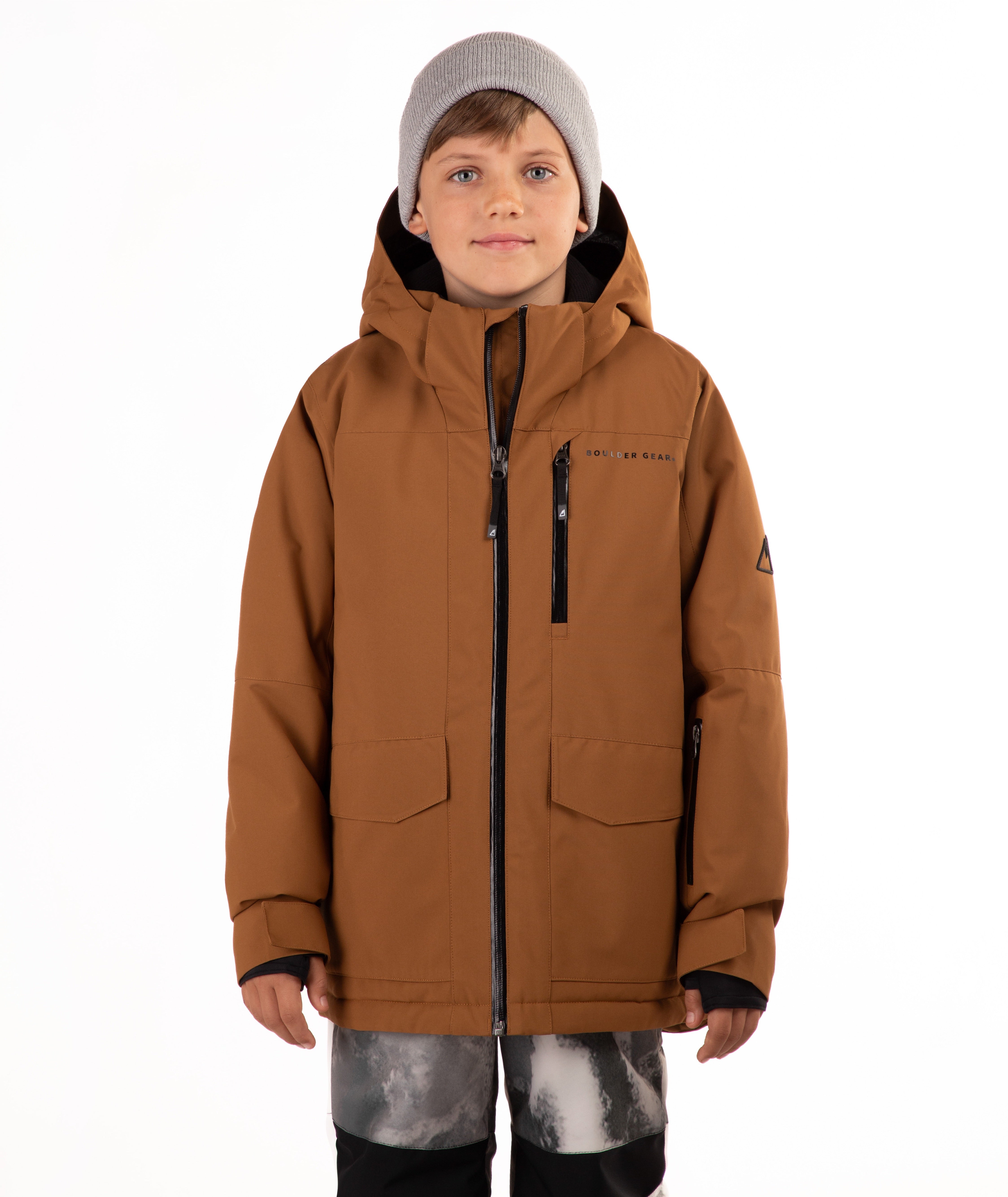 A child wearing a brown hooded snowboard jacket with black zippers, a gray beanie, and patterned pants, standing against a plain white background.